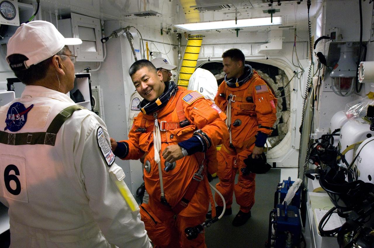 KENNEDY SPACE CENTER, FLA. -- In the White Room on Launch Pad 39A at NASA's Kennedy Space Center, STS-120 Mission Specialist Daniel Tani is helped by the closeout crew to put on a parachute and get ready to enter space shuttle Discovery for liftoff at 11:38 a.m. EDT.  Behind him is Mission Specialist Doug Wheelock.  At the end of the mission, Tani will remain behind on the International Space Station to join the Expedition 16 crew.   The STS-120 mission will be the 23rd assembly flight to the space station and the 34th flight for Discovery.  Payload on the mission is the Italian-built U.S. Node 2, called Harmony.  During the 14-day mission, the crew will install Harmony and move the P6 solar arrays to their permanent position and deploy them.  Discovery is expected to complete its mission and return home at 4:47 a.m. EST on Nov. 6.   Photo credit: NASA/Scott Haun, Tom Farrar, Rafael Hernandez
