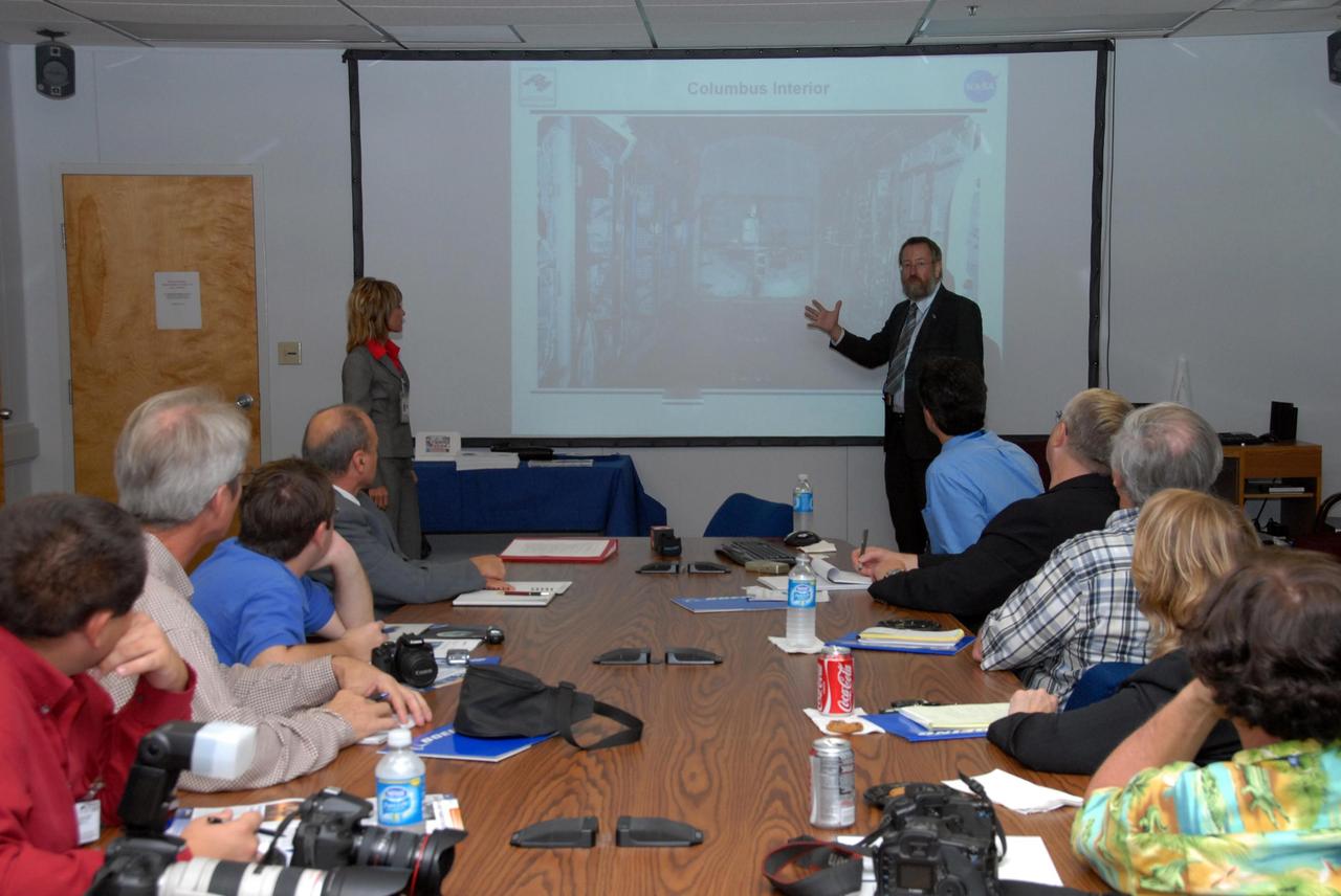 KENNEDY SPACE CENTER, FLA. -- Prior to a showing of the European Space Agency's  Columbus Laboratory module, Gregor Woop, in front of the screen, provides information about the module for the media gathered at the table.  Woop is the European Space Agency's product assurance and safety manager. Standing at left is Debbie Hahn, NASA mission manager.  Columbus is the European Space Agency 's largest single contribution to the International Space Station.  The laboratory module will expand the research facilities of the station, providing crew members and scientists around the world the ability to conduct a variety of life, physical and materials science experiments. The module is approximately 23 feet long and 15 feet wide, allowing it to hold 10 large racks of experiments. Columbus is scheduled to be transferred to Launch Pad 39A in early November, in preparation for its journey to the station. Columbus will fly aboard space shuttle Atlantis on the STS-122 mission, targeted for launch Dec. 6.  Photo credit: NASA/George Shelton