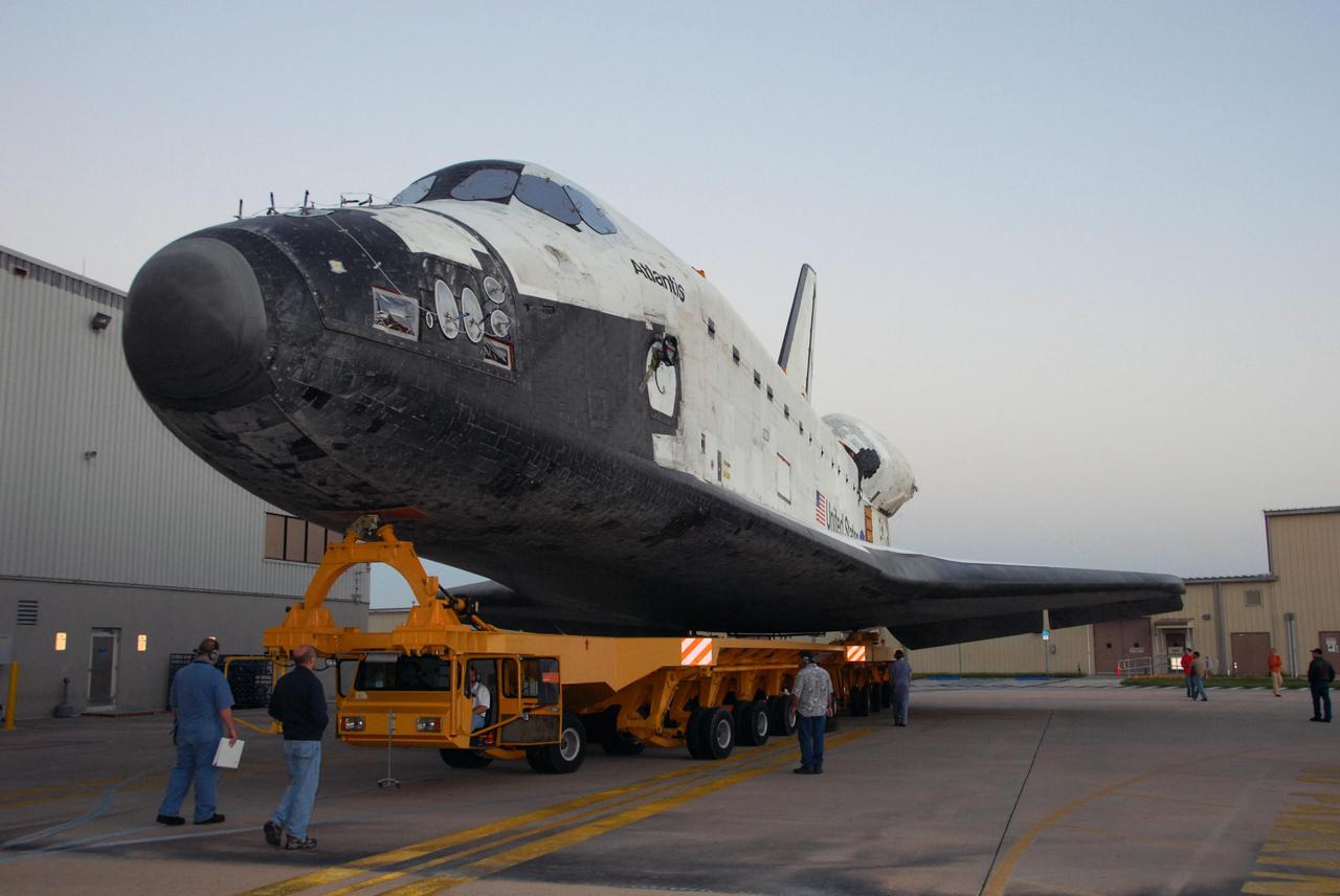 KENNEDY SPACE CENTER, FLA. -- As the sun rises, workers accompany space shuttle Atlantis as it rolls out of Orbiter Processing Facility bay 1 on a transporter.  The orbiter is headed for the Vehicle Assembly Building.  Rollover from its processing bay began at 7:05 a.m. EDT. Atlantis arrived in the VAB's transfer aisle at 8:03 a.m. In the VAB, the shuttle will be lifted and mated with the external tank and solid rocket boosters designated for mission STS-122, already secured atop a mobile launcher platform.  On this mission, Atlantis will deliver the Columbus module to the International Space Station.  The European Space Agency's largest contribution to the station, Columbus is a multifunctional, pressurized laboratory that will be permanently attached to U.S. Node 2, called Harmony. The module is approximately 23 feet long and 15 feet wide, allowing it to hold 10 large racks of experiments.  The laboratory will expand the research facilities aboard the station, providing crew members and scientists from around the world the ability to conduct a variety of experiments in the physical, materials and life sciences.  Mission STS-122 is targeted for launch on Dec. 6.  Photo credit: NASA/George Shelton