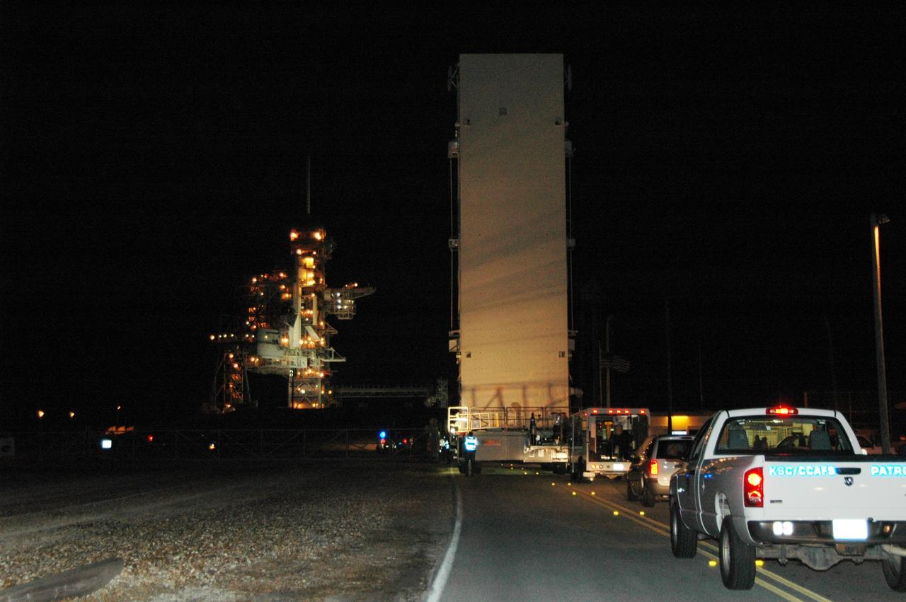 KENNEDY SPACE CENTER, FLA. -- At NASA's Kennedy Space Center, the payload canister atop its transporter rolls, under escort, toward Launch Pad 39A, seen at left.The canister contains the Columbus Lab module and integrated cargo carrier-lite payloads for space shuttle Atlantis on mission STS-122.  They will be transferred into the payload changeout room on the pad. Atlantis is targeted to launch on Dec. 6.  Photo credit: NASA/Dimitri Gerondidakis