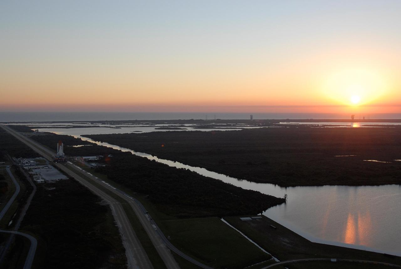 KENNEDY SPACE CENTER, FLA. -- Space Shuttle Atlantis, atop a mobile launch platform, passes by the turn basin in Launch Complex 39 toward Pad A as the sun rises on a balmy Florida morning. First motion out of the VAB was at 4:43 a.m. EST. Rollout is a milestone for Atlantis' launch to the International Space Station on mission STS-122, targeted for Dec. 6. On this mission, Atlantis will deliver the Columbus module to the International Space Station. The European Space Agency's largest contribution to the station, Columbus is a multifunctional, pressurized laboratory that will be permanently attached to U.S. Node 2, called Harmony. The module is approximately 23 feet long and 15 feet wide, allowing it to hold 10 large racks of experiments. The laboratory will expand the research facilities aboard the station, providing crew members and scientists from around the world the ability to conduct a variety of experiments in the physical, materials and life sciences. Photo credit: NASA/Kim Shiflett