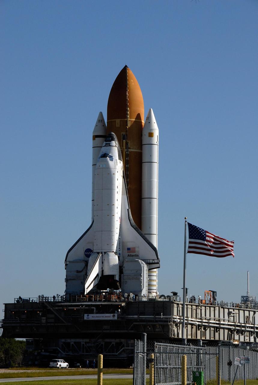 KENNEDY SPACE CENTER, FLA. -- Space Shuttle Atlantis, secured atop a mobile launch platform, passes by a United States flag on its way to Launch Pad 39A on a breezy Florida morning. The crawler transporter has a top speed of one mile per hour while it is moving the space shuttle. First motion out of the Vehicle Assembly Building was at 4:43 a.m. EST. Rollout is a milestone for Atlantis' launch to the International Space Station on mission STS-122, targeted for Dec. 6. On this mission, Atlantis will deliver the Columbus module to the International Space Station. The European Space Agency's largest contribution to the station, Columbus is a multifunctional, pressurized laboratory that will be permanently attached to U.S. Node 2, called Harmony. The module is approximately 23 feet long and 15 feet wide, allowing it to hold 10 large racks of experiments. The laboratory will expand the research facilities aboard the station, providing crew members and scientists from around the world the ability to conduct a variety of experiments in the physical, materials and life sciences. Photo credit: NASA/Kim Shiflett