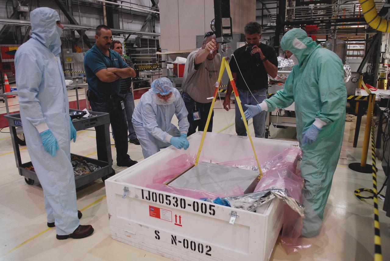 KENNEDY SPACE CENTER, FLA. -- In the Orbiter Processing Facility, technicians get ready to remove one of two Materials International Space Station Experiments, or MISSE, from a shipping container. The MISSE is part of the payload onboard space shuttle Endeavour for mission STS-123. It will be installed in Endeavour's payload bay. The MISSE project is a NASA/Langley Research Center-managed cooperative endeavor to fly materials and other types of space exposure experiments on the International Space Station. The objective is to develop early, low-cost, non-intrusive opportunities to conduct critical space exposure tests of space materials and components planned for use on future spacecraft. Photo credit: NASA/Kim Shiflett