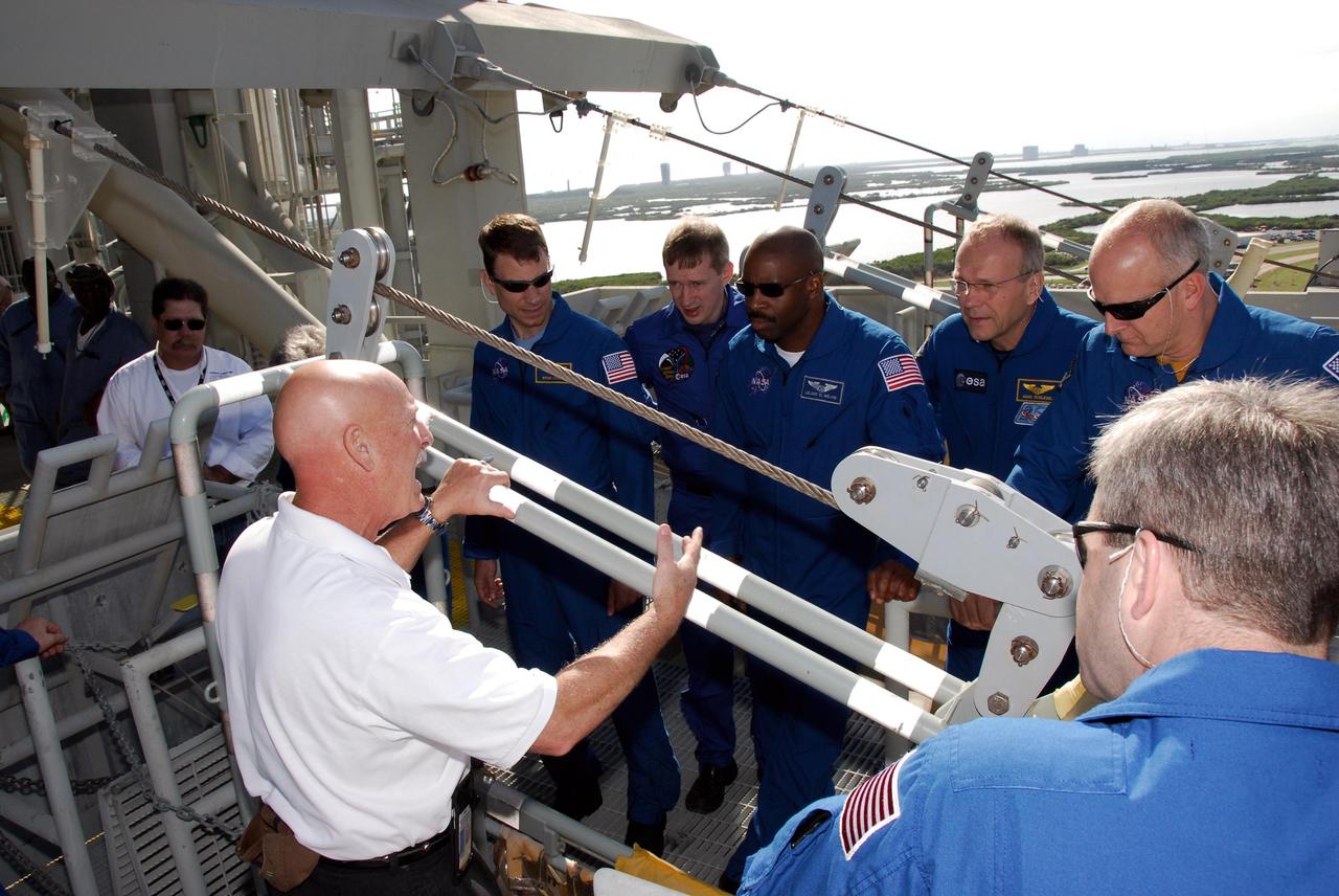 KENNEDY SPACE CENTER, FLA. -- The space shuttle Atlantis STS-122 crew receives instruction on slidewire basket operation, part of the emergency exit system on the fixed service structure on Launch Pad 39A. From left are Mission Specialists Stanley Love; Leopold Eyharts' backup, Frank De Winne; Leland Melvin and Hans Schlegel; Pilot Alan Poindexter; and Commander Steve Frick, with his back to the camera. Schlegel, Eyharts and De Winne are with the European Space Agency. Eyharts will remain on the International Space Station as a flight engineer for Expedition 16 following the STS-122 mission. Seven slidewire baskets are available to carry the crew from the level of the pad's Orbiter Access Arm to a safe landing site below, if needed. Each basket can hold up to three people. A braking system catch net and drag chain slow, and then halt, the baskets as they travel down the wire at approximately 55 miles per hour. The journey takes about half a minute. A bunker is located in the landing zone 1,200 feet west of the pad, with an M-113 armored personnel carrier stationed nearby. The STS-122 crew is at NASA's Kennedy Space Center to take part in terminal countdown demonstration test, or TCDT, activities, a standard part of launch preparations. The TCDT provides astronauts and ground crews with equipment familiarization and a simulated launch countdown before launch. On mission STS-122, Atlantis will deliver the European Space Agency's Columbus module to the International Space Station. Columbus is a multifunctional, pressurized laboratory that will be permanently attached to U.S. Node 2, called Harmony, and will expand the research facilities aboard the station. Launch is targeted for Dec. 6. Photo credit: NASA/Kim Shiflett