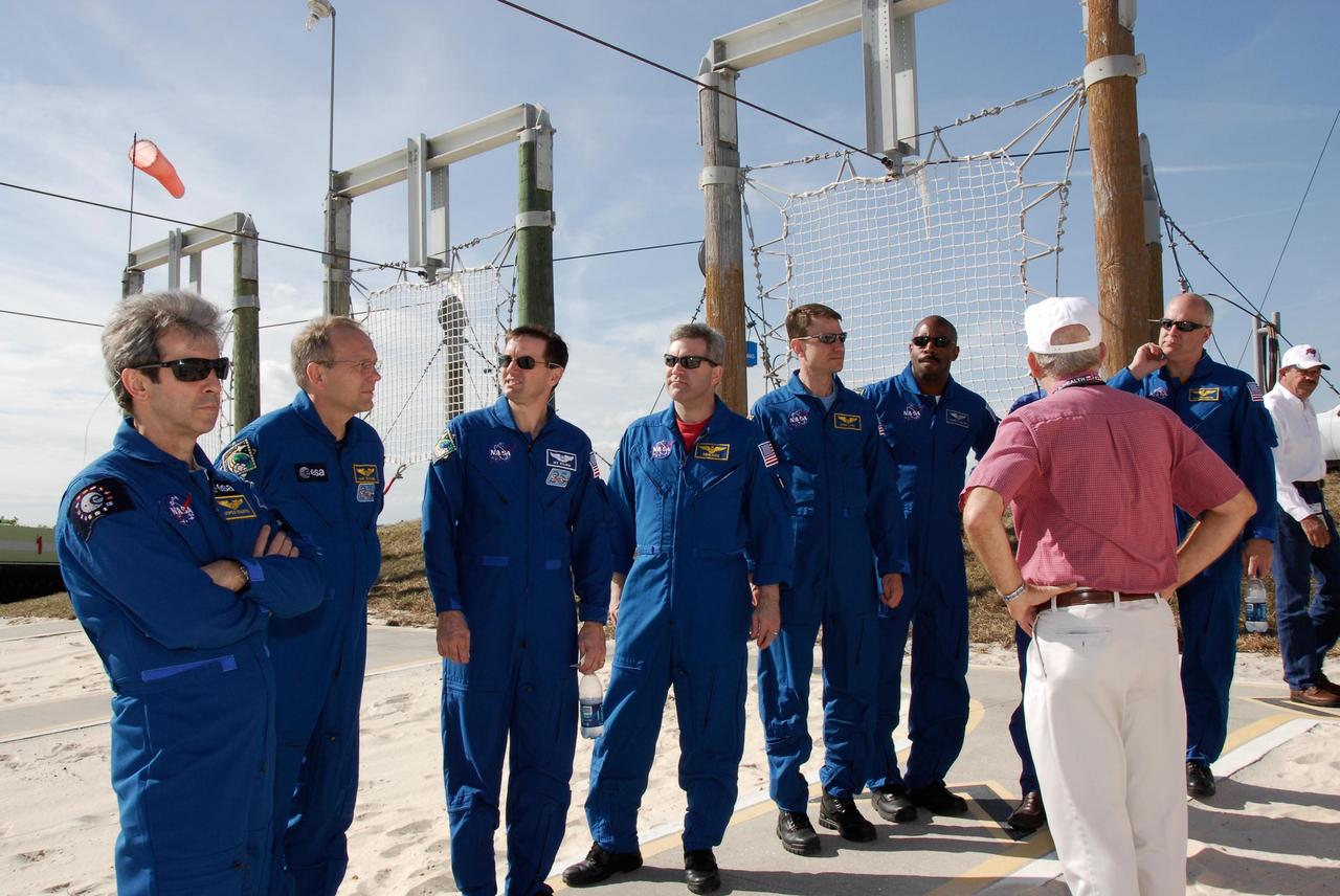 KENNEDY SPACE CENTER, FLA. -- The space shuttle Atlantis STS-122 crew receives instruction on slidewire basket operation, part of the emergency exit system on the fixed service structure on Launch Pad 39A. Seen here near the catch nets in the landing zone are, from left, Mission Specialists Leopold Eyharts, Hans Schlegel and Rex Walheim; Commander Steve Frick; Mission Specialists Stanley Love and Leland Melvin; and Pilot Alan Poindexter. Seven slidewire baskets are available to carry the crew from the level of the pad's Orbiter Access Arm to this landing site, if needed. Each basket can hold up to three people. A braking system catch net and drag chain slow, and then halt, the baskets as they travel down the wire at approximately 55 miles per hour. The journey takes about half a minute. A bunker is located in the landing zone 1,200 feet west of the pad, with an M-113 armored personnel carrier stationed nearby. The STS-122 crew is at NASA's Kennedy Space Center to take part in terminal countdown demonstration test, or TCDT, activities, a standard part of launch preparations. The TCDT provides astronauts and ground crews with equipment familiarization and a simulated launch countdown before launch. On mission STS-122, Atlantis will deliver the European Space Agency's Columbus module to the International Space Station. Columbus is a multifunctional, pressurized laboratory that will be permanently attached to U.S. Node 2, called Harmony, and will expand the research facilities aboard the station. Launch is targeted for Dec. 6. Photo credit: NASA/Kim Shiflett