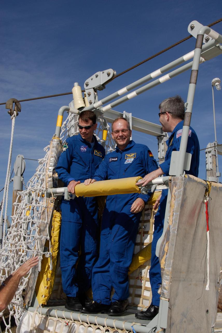 KENNEDY SPACE CENTER, FLA. -- The space shuttle Atlantis STS-122 crew receives instruction on slidewire basket operation, part of the emergency exit system on the fixed service structure on Launch Pad 39A. From left, Mission Specialists Stanley Love and Hans Schlegel and Commander Steve Frick gain first-hand experience inside one of the baskets. Seven slidewire baskets are available to carry the crew from the level of the pad's Orbiter Access Arm to this landing site, if needed. Each basket can hold up to three people. A braking system catch net and drag chain slow, and then halt, the baskets as they travel down the wire at approximately 55 miles per hour. The journey takes about half a minute. A bunker is located in the landing zone 1,200 feet west of the pad, with an M-113 armored personnel carrier stationed nearby. The STS-122 crew is at NASA's Kennedy Space Center to take part in terminal countdown demonstration test, or TCDT, activities, a standard part of launch preparations. The TCDT provides astronauts and ground crews with equipment familiarization and a simulated launch countdown before launch. On mission STS-122, Atlantis will deliver the European Space Agency's Columbus module to the International Space Station. Columbus is a multifunctional, pressurized laboratory that will be permanently attached to U.S. Node 2, called Harmony, and will expand the research facilities aboard the station. Launch is targeted for Dec. 6. Photo credit: NASA/Kim Shiflett