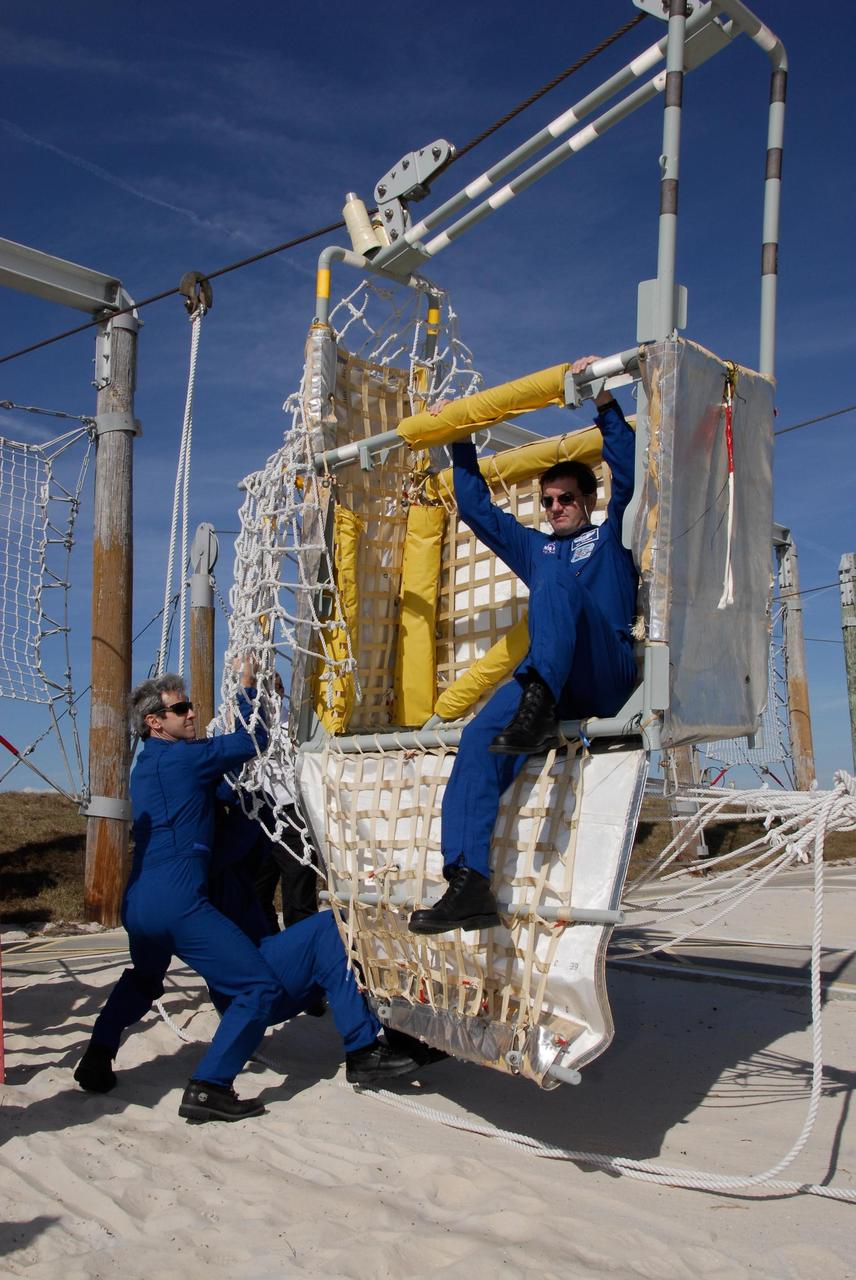 KENNEDY SPACE CENTER, FLA. -- The space shuttle Atlantis STS-122 crew receives instruction on slidewire basket operation, part of the emergency exit system on the fixed service structure on Launch Pad 39A. Here, Mission Specialist Rex Walheim practices getting out of one of the baskets as Mission Specialists Leopold Eyharts and Leland Melvin steady it. Seven slidewire baskets are available to carry the crew from the level of the pad's Orbiter Access Arm to this landing site, if needed. Each basket can hold up to three people. A braking system catch net and drag chain slow, and then halt, the baskets as they travel down the wire at approximately 55 miles per hour. The journey takes about half a minute. A bunker is located in the landing zone 1,200 feet west of the pad, with an M-113 armored personnel carrier stationed nearby. The STS-122 crew is at NASA's Kennedy Space Center to take part in terminal countdown demonstration test, or TCDT, activities, a standard part of launch preparations. The TCDT provides astronauts and ground crews with equipment familiarization and a simulated launch countdown before launch. On mission STS-122, Atlantis will deliver the European Space Agency's Columbus module to the International Space Station. Columbus is a multifunctional, pressurized laboratory that will be permanently attached to U.S. Node 2, called Harmony, and will expand the research facilities aboard the station. Launch is targeted for Dec. 6. Photo credit: NASA/Kim Shiflett
