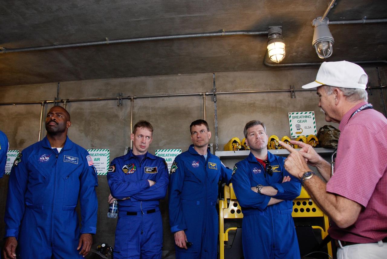 KENNEDY SPACE CENTER, FLA. -- The space shuttle Atlantis STS-122 crew receives instruction on the emergency exit system on Launch Pad 39A. Inside the bunker at the foot of the pad, from left, Mission Specialist Leland Melvin; astronaut Frank De Winne of the European Space Agency, backup for Expedition 16 Flight Engineer Leopold Eyharts; Mission Specialist Stanley Love; and Commander Steve Frick listen intently to their trainer. Seven slidewire baskets are available to carry the crew from the level of the pad's Orbiter Access Arm to a safe landing site below, if needed. Each basket can hold up to three people. A braking system catch net and drag chain slow, and then halt, the baskets as they travel down the wire at approximately 55 miles per hour. The journey takes about half a minute. A bunker is located in the landing zone 1,200 feet west of the pad, with an M-113 armored personnel carrier stationed nearby. The STS-122 crew is at NASA's Kennedy Space Center to take part in terminal countdown demonstration test, or TCDT, activities, a standard part of launch preparations. The TCDT provides astronauts and ground crews with equipment familiarization and a simulated launch countdown before launch. On mission STS-122, Atlantis will deliver the European Space Agency's Columbus module to the International Space Station. Columbus is a multifunctional, pressurized laboratory that will be permanently attached to U.S. Node 2, called Harmony, and will expand the research facilities aboard the station. Launch is targeted for Dec. 6. Photo credit: NASA/Kim Shiflett