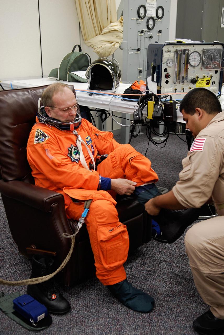 KENNEDY SPACE CENTER, FLA. -- A suit technician helps space shuttle Atlantis STS-122 Mission Specialist Hans Schlegel put on his launch and entry suit, in astronaut crew quarters. Schlegel is with the European Space Agency. The STS-122 crew is preparing for a simulated launch countdown aboard Atlantis, part of terminal countdown demonstration test, or TCDT, activities at NASA's Kennedy Space Center. The TCDT is a dress rehearsal for launch and also provides astronauts and ground crews with equipment familiarization and emergency egress training. On mission STS-122, Atlantis will deliver the Columbus module to the International Space Station. The European Space Agency's largest single contribution to the station, Columbus is a multifunctional, pressurized laboratory that will be permanently attached to U.S. Node 2, called Harmony. The laboratory will expand the research facilities aboard the station, providing crew members and scientists from around the world the ability to conduct a variety of experiments in the physical, materials and life sciences. Launch is targeted for Dec. 6. Photo credit: NASA/Kim Shiflett