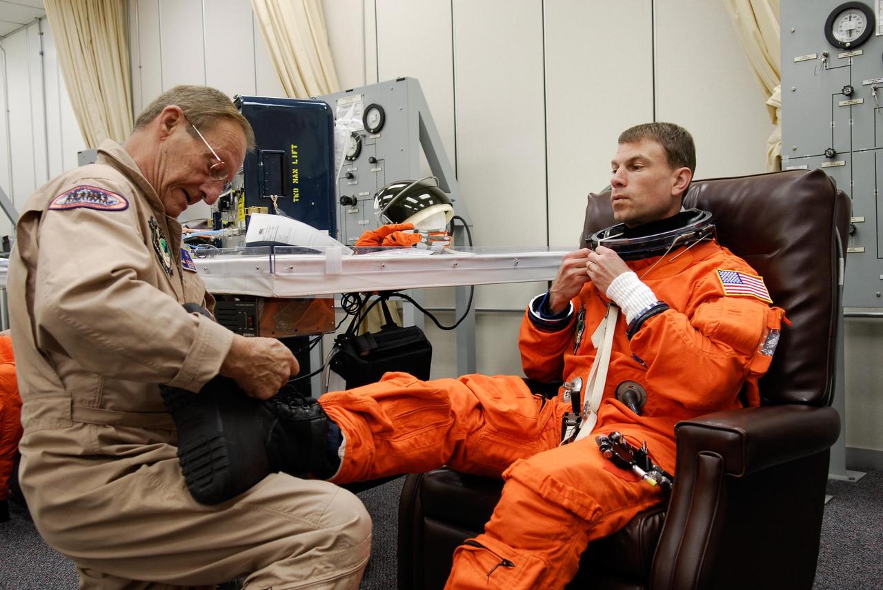 KENNEDY SPACE CENTER, FLA. -- A suit technician helps space shuttle Atlantis STS-122 Mission Specialist Stanley Love lace his boots, part of his launch and entry suit, in astronaut crew quarters. The STS-122 crew is preparing for a simulated launch countdown aboard Atlantis, part of terminal countdown demonstration test, or TCDT, activities at NASA's Kennedy Space Center. The TCDT is a dress rehearsal for launch and also provides astronauts and ground crews with equipment familiarization and emergency egress training. On mission STS-122, Atlantis will deliver the Columbus module to the International Space Station. The European Space Agency's largest single contribution to the station, Columbus is a multifunctional, pressurized laboratory that will be permanently attached to U.S. Node 2, called Harmony. The laboratory will expand the research facilities aboard the station, providing crew members and scientists from around the world the ability to conduct a variety of experiments in the physical, materials and life sciences. Launch is targeted for Dec. 6. Photo credit: NASA/Kim Shiflett