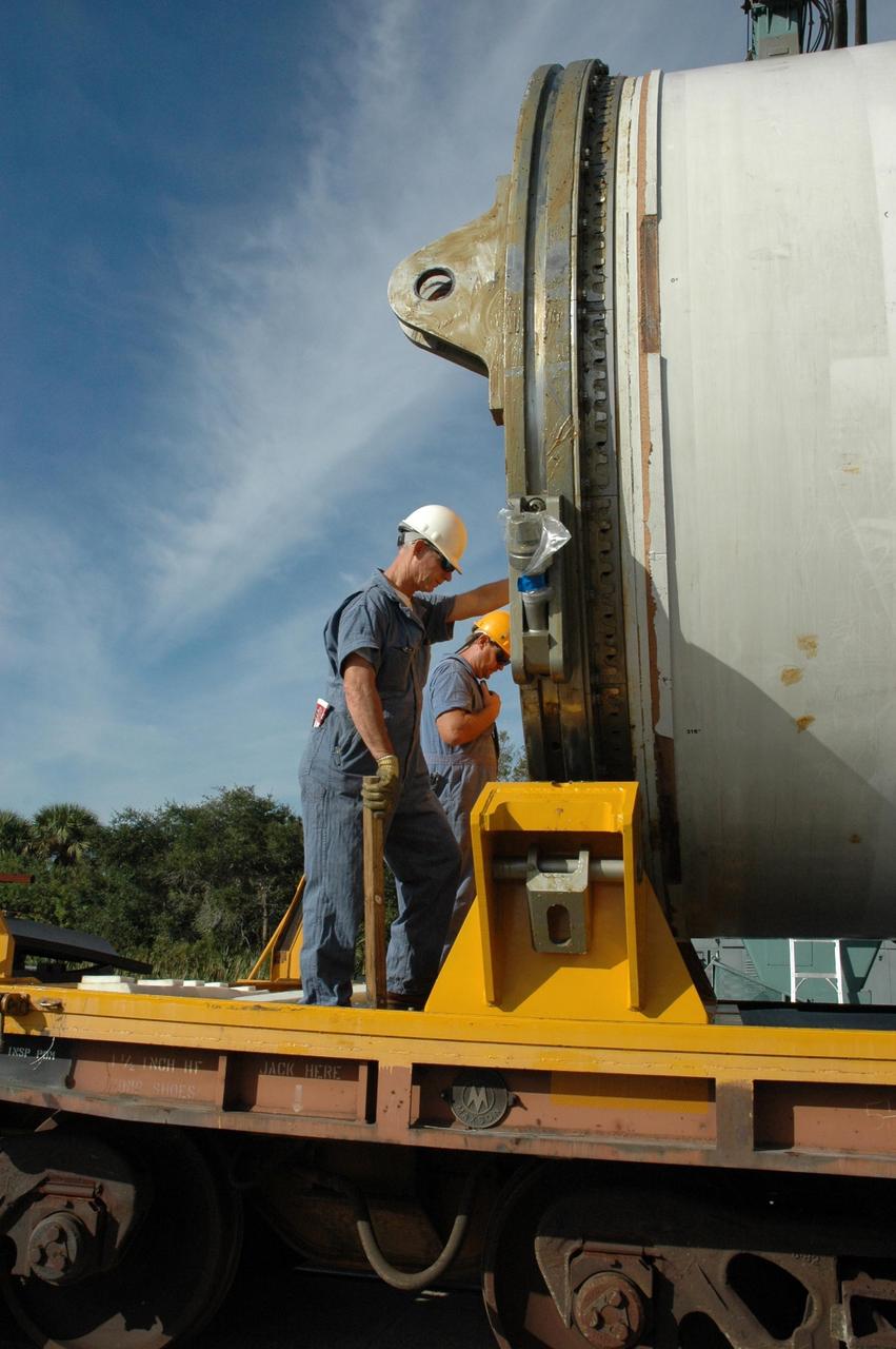KENNEDY SPACE CENTER, FLA. --  Workers oversee the placement of a solid rocket booster segment onto a railroad car at the railroad yard at NASA's Kennedy Space Center.  The spent segment is part of the booster used to launch space shuttle Discovery in October. The segment will be placed on the car and covered for the long trip back to Utah.  After a mission, the spent boosters are recovered, cleaned, disassembled, refurbished and reused after each launch. After hydrolasing the interior of each segment, they are placed on flatbed trucks.  The individual booster segments are transferred to a railhead located at the railroad yard at NASA's Kennedy Space Center. The long train of segments is part of the twin solid rocket boosters used to launch space shuttle Discovery in October.  The NASA Railroad locomotive backs up the rail cars and the segment is lowered onto the car. The covered segments are moved to Titusville for interchange with Florida East Coast Railway to begin the trip back to Utah.  Photo credit: NASA/Amanda Diller