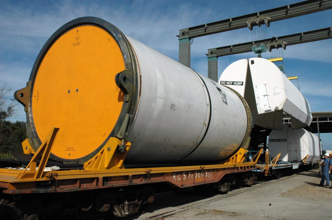 KENNEDY SPACE CENTER, FLA. --  At the railroad yard at NASA's Kennedy Space Center, covers are being placed over solid rocket booster segments that will be transported to Utah.  The yellow transportation end covers have already been inserted and are secure, as seen on the segment at left.  The spent segments are part of the booster used to launch space shuttle Discovery in October.   After a mission, the spent boosters are recovered, cleaned, disassembled, refurbished and reused after each launch. After hydrolasing the interior of each segment, they are placed on flatbed trucks.  The individual booster segments are transferred to a railhead located at the railroad yard at NASA's Kennedy Space Center. The long train of segments is part of the twin solid rocket boosters used to launch space shuttle Discovery in October.  The NASA Railroad locomotive backs up the rail cars and the segment is lowered onto the car. The covered segments are moved to Titusville for interchange with Florida East Coast Railway to begin the trip back to Utah.  Photo credit: NASA/Amanda Diller