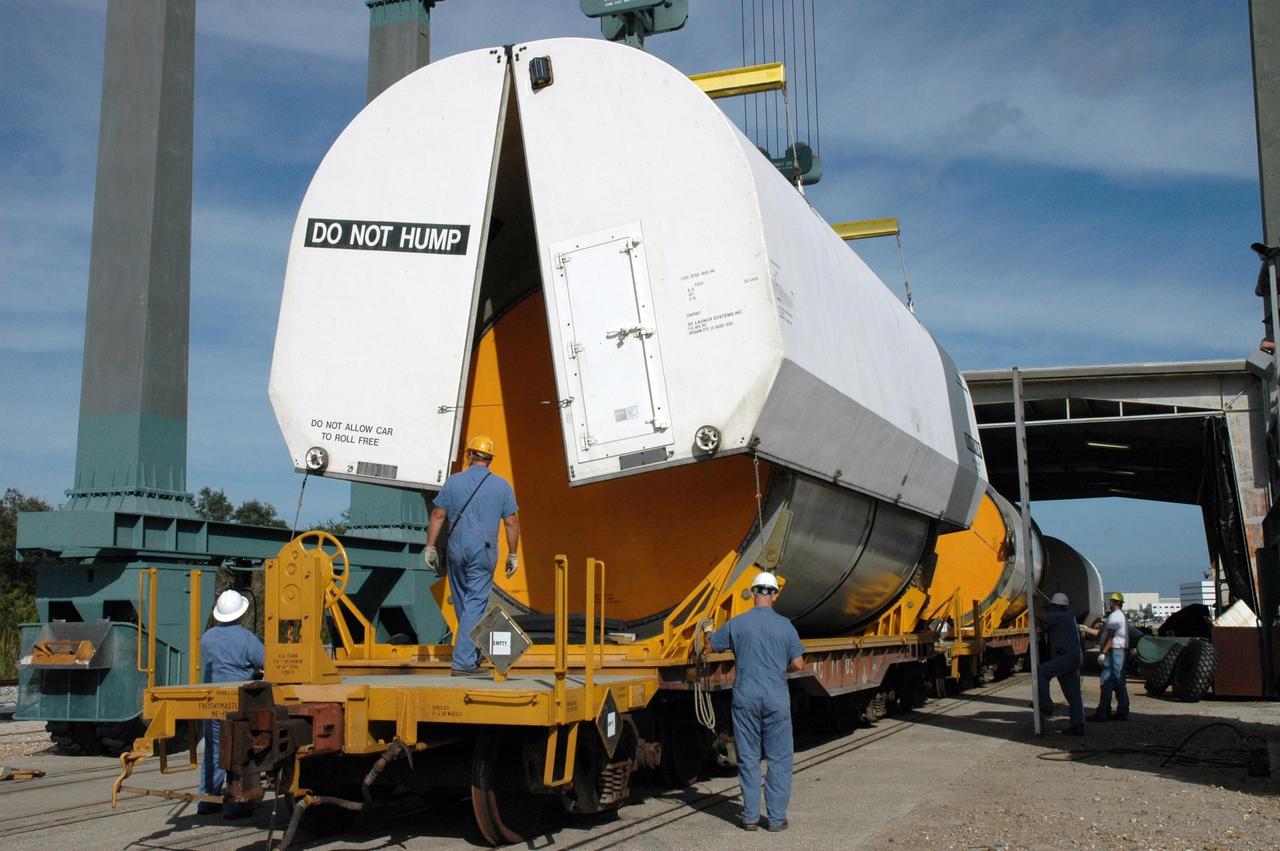 KENNEDY SPACE CENTER, FLA. --  Workers at the railroad yard at NASA's Kennedy Space Center stand ready to secure the transportation cover over the solid rocket booster segment that is being transported to Utah.  The spent segments are part of the booster used to launch space shuttle Discovery in October.   After a mission, the spent boosters are recovered, cleaned, disassembled, refurbished and reused after each launch. After hydrolasing the interior of each segment, they are placed on flatbed trucks.  The individual booster segments are transferred to a railhead located at the railroad yard at NASA's Kennedy Space Center. The long train of segments is part of the twin solid rocket boosters used to launch space shuttle Discovery in October.  The NASA Railroad locomotive backs up the rail cars and the segment is lowered onto the car. The covered segments are moved to Titusville for interchange with Florida East Coast Railway to begin the trip back to Utah.  Photo credit: NASA/Amanda Diller