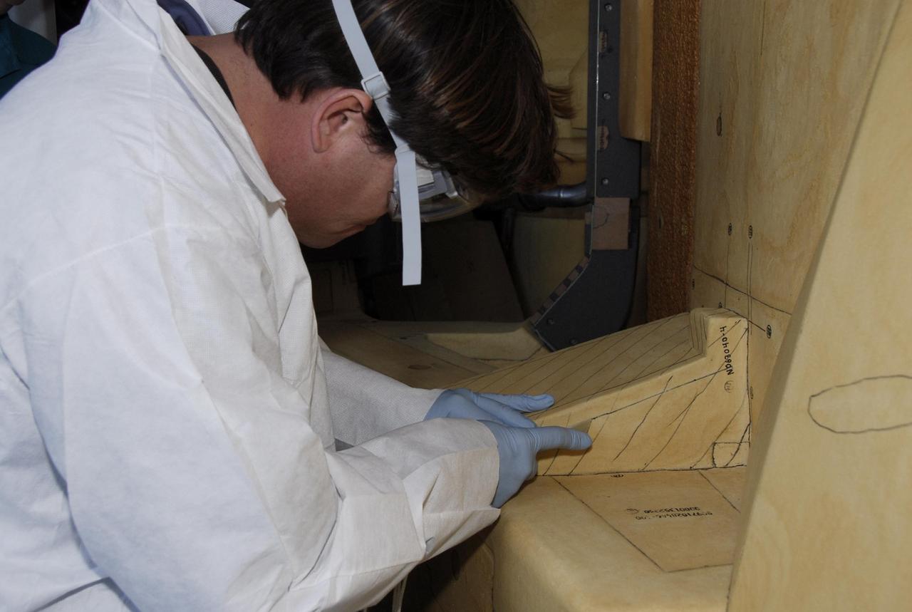 KENNEDY SPACE CENTER, FLA. -- At Launch Pad 39A, a United Space Alliance technician carefully cuts away the foam insulation surrounding the covers over the feed-through connector box on the external tank for space shuttle Atlantis' STS-122 mission. The covers will be removed for access to the feed-through connectors.  Following the failure of some of the tank's engine cutoff sensors, or ECO sensors, during propellant tanking for launch attempts on Dec. 6 and Dec. 9, a tanking test was conducted on Dec. 18 to aid in troubleshooting the cause. Technicians spliced test wiring into the ECO sensor electrical system and used time domain reflectometry equipment to help locate the electrical anomaly. Results of the tanking test pointed to an open circuit in the feed-through connector wiring, which is located at the base of the tank. The feed-through connector passes the wires from the inside of the tank to the outside.  During the holiday period, workers from Lockheed Martin will begin inspecting and testing the connector.  Shuttle program managers will meet on Dec. 27 to review the test and analysis, and decide on a forward plan.  Photo credit: NASA/Kim Shiflett