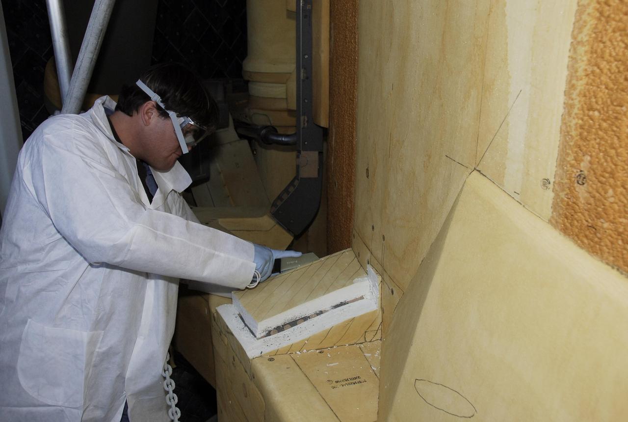 KENNEDY SPACE CENTER, FLA. -- At Launch Pad 39A, a United Space Alliance technician carefully cuts away the foam insulation surrounding the covers over the feed-through connector box on the external tank for space shuttle Atlantis' STS-122 mission, revealing the fastener holes on the covers.  The covers will be removed for access to the feed-through connectors.  Following the failure of some of the tank's engine cutoff sensors, or ECO sensors, during propellant tanking for launch attempts on Dec. 6 and Dec. 9, a tanking test was conducted on Dec. 18 to aid in troubleshooting the cause. Technicians spliced test wiring into the ECO sensor electrical system and used time domain reflectometry equipment to help locate the electrical anomaly. Results of the tanking test pointed to an open circuit in the feed-through connector wiring, which is located at the base of the tank. The feed-through connector passes the wires from the inside of the tank to the outside.  During the holiday period, workers from Lockheed Martin will begin inspecting and testing the connector.  Shuttle program managers will meet on Dec. 27 to review the test and analysis, and decide on a forward plan.  Photo credit: NASA/Kim Shiflett
