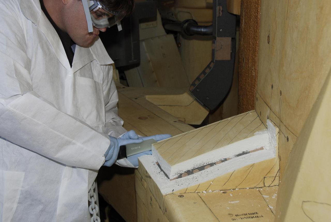 KENNEDY SPACE CENTER, FLA. -- At Launch Pad 39A, a United Space Alliance technician carefully cuts away the foam insulation surrounding the covers over the feed-through connector box on the external tank for space shuttle Atlantis' STS-122 mission, revealing the fastener holes on the covers.  The covers will be removed for access to the feed-through connectors.  Following the failure of some of the tank's engine cutoff sensors, or ECO sensors, during propellant tanking for launch attempts on Dec. 6 and Dec. 9, a tanking test was conducted on Dec. 18 to aid in troubleshooting the cause. Technicians spliced test wiring into the ECO sensor electrical system and used time domain reflectometry equipment to help locate the electrical anomaly. Results of the tanking test pointed to an open circuit in the feed-through connector wiring, which is located at the base of the tank. The feed-through connector passes the wires from the inside of the tank to the outside.  During the holiday period, workers from Lockheed Martin will begin inspecting and testing the connector.  Shuttle program managers will meet on Dec. 27 to review the test and analysis, and decide on a forward plan.  Photo credit: NASA/Kim Shiflett