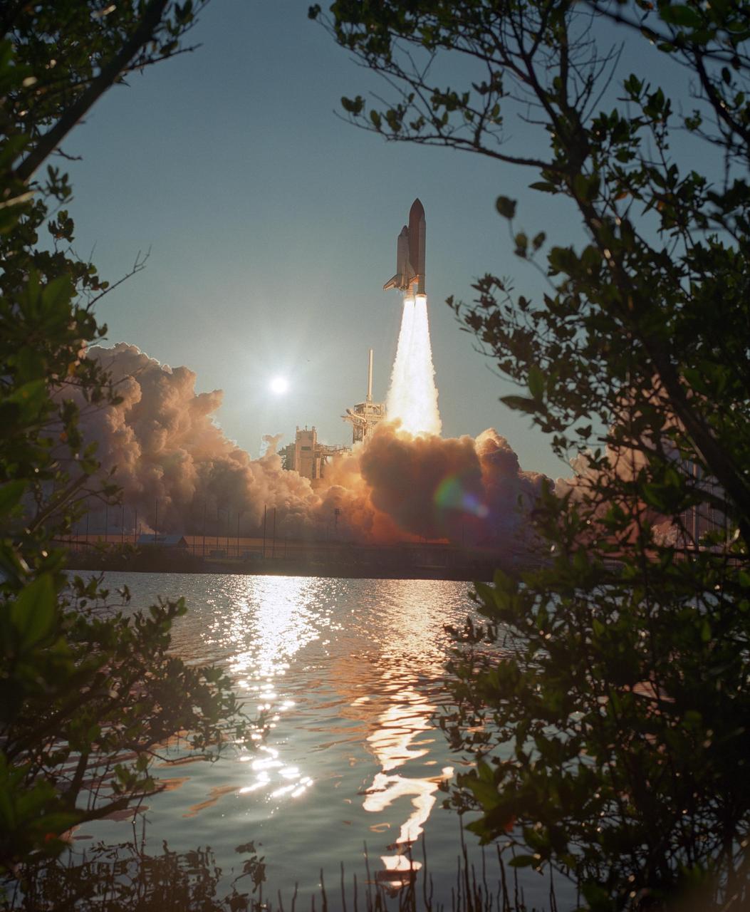 KENNEDY SPACE CENTER, FLA. --   Branches on the near bank frame the image of Space Shuttle Atlantis as it leaps free of the clouds of smoke and steam, colored by the setting sun, billowing across Launch Pad 39A. The launch nearly eclipses the sun, seen above the service structure at left. Liftoff of Atlantis on mission STS-117 to the International Space Station was on-time at 7:38:04 p.m. EDT. The shuttle is delivering a new segment to the starboard side of the International Space Station's backbone, known as the truss. Three spacewalks are planned to install the S3/S4 truss segment, deploy a set of solar arrays and prepare them for operation. STS-117 is the 118th space shuttle flight, the 21st flight to the station, the 28th flight for Atlantis and the first of four flights planned for 2007. Photo Credit:  NASA/Sandra Joseph and Robert Murray