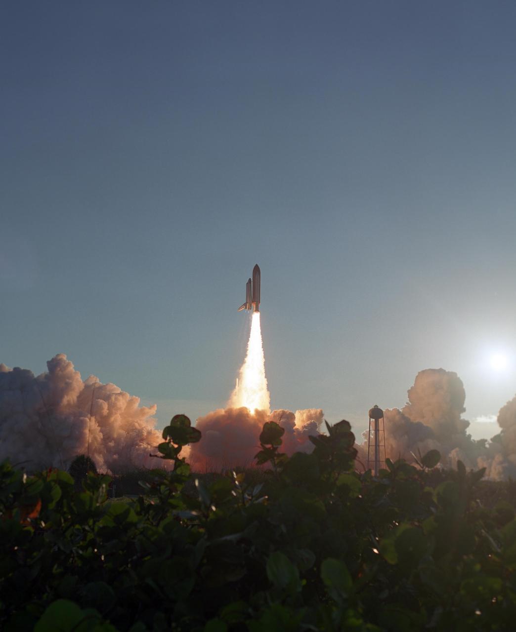 KENNEDY SPACE CENTER, FLA. --  Shrubbery is cast in shadow as the launch of Space Shuttle Atlantis lights up the sky behind it.  The liftoff at 7:38:04 p.m. EDT created masses of smoke and steam clouds painted with sunset hues as they roll across Launch Pad 39A.  Atlantis launched on time for its mission STS-117 to the International Space Station. The shuttle is delivering a new segment to the starboard side of the International Space Station's backbone, known as the truss. Three spacewalks are planned to install the S3/S4 truss segment, deploy a set of solar arrays and prepare them for operation. STS-117 is the 118th space shuttle flight, the 21st flight to the station, the 28th flight for Atlantis and the first of four flights planned for 2007.   Photo credit: NASA/Sandra Joseph & Robert Murray