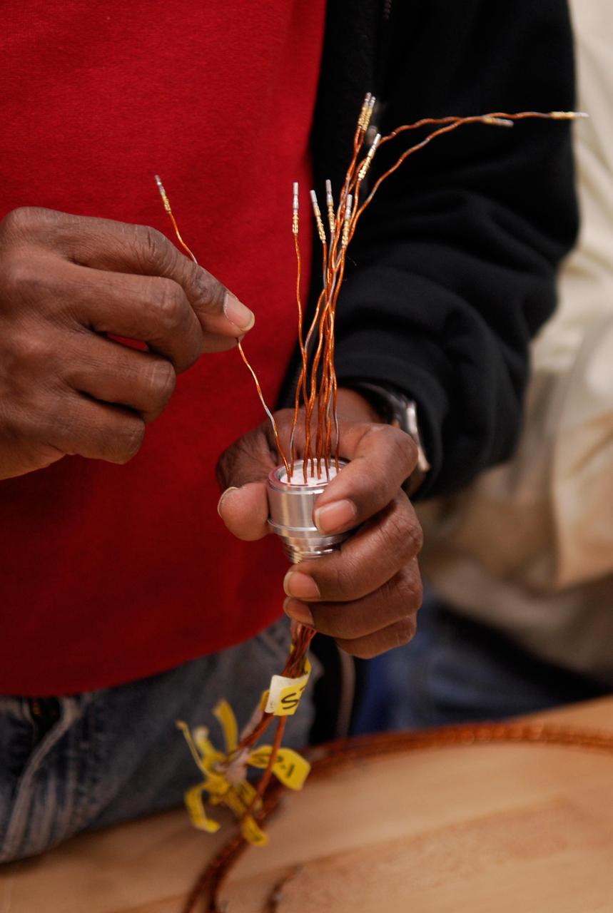 KENNEDY SPACE CENTER, FLA. -- At a lab at NASA's Kennedy Space Center, a Lockheed Martin technician prepares an electrical wiring harness during a procedure to solder the pins to the socket of the replacement feed-through connector that will be installed in the external fuel tank for space shuttle Atlantis' STS-122 mission. Two United Launch Alliance technicians, who performed this exacting task on the Centaur upper stage for Atlas and Titan launches in 1994, will be doing the soldering.   Soldering the connector pins and sockets together addresses the most likely cause of a problem in the engine cutoff sensor system, or ECO system.  Some of the tank's ECO sensors failed during propellant tanking for launch attempts on Dec. 6 and Dec. 9.  Results of a tanking test on Dec. 18 pointed to an open circuit in the feed-through connector wiring, which is located at the base of the tank. The feed-through connector passes the wires from the inside of the tank to the outside.  After the soldering is completed and the connector is reinstalled, shuttle program managers will decide on how to proceed.  The launch date for mission STS-122 is under review.  Photo credit: NASA/Kim Shiflett