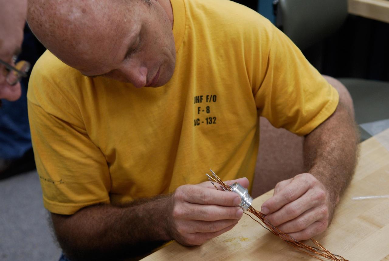 KENNEDY SPACE CENTER, FLA. -- At a lab at NASA's Kennedy Space Center, Kevin Wyckoff, an aerospace technician with the United Launch Alliance, examines an electrical wiring harness.  The harness will be inserted into a replacement feed-through connector during preparations to solder the pins to the socket of the connector. The connector will later be installed in the external fuel tank for space shuttle Atlantis' STS-122 mission. The technician performed this exacting task on the Centaur upper stage for Atlas and Titan launches in 1994 and was specifically chosen for the task.   Soldering the connector pins and sockets together addresses the most likely cause of a problem in the engine cutoff sensor system, or ECO system.  Some of the tank's ECO sensors failed during propellant tanking for launch attempts on Dec. 6 and Dec. 9.  Results of a tanking test on Dec. 18 pointed to an open circuit in the feed-through connector wiring, which is located at the base of the tank. The feed-through connector passes the wires from the inside of the tank to the outside.  After the soldering is completed and the connector is reinstalled, shuttle program managers will decide on how to proceed.  The launch date for mission STS-122 is under review.  Photo credit: NASA/Kim Shiflett