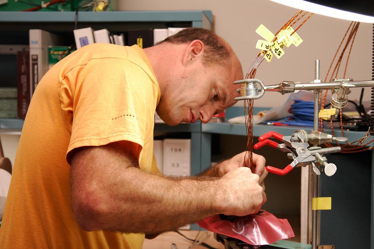 KENNEDY SPACE CENTER, FLA. -- At a lab at NASA's Kennedy Space Center, Kevin Wyckoff, an aerospace technician with the United Launch Alliance, inserts an electrical wiring harness into a replacement feed-through connector during preparations to solder the pins to the socket of the connector. The connector will later be installed in the external fuel tank for space shuttle Atlantis' STS-122 mission. The technician performed this exacting task on the Centaur upper stage for Atlas and Titan launches in 1994 and was specifically chosen for the task.   Soldering the connector pins and sockets together addresses the most likely cause of a problem in the engine cutoff sensor system, or ECO system.  Some of the tank's ECO sensors failed during propellant tanking for launch attempts on Dec. 6 and Dec. 9.  Results of a tanking test on Dec. 18 pointed to an open circuit in the feed-through connector wiring, which is located at the base of the tank. The feed-through connector passes the wires from the inside of the tank to the outside.  After the soldering is completed and the connector is reinstalled, shuttle program managers will decide on how to proceed.  The launch date for mission STS-122 is under review.  Photo credit: NASA/Kim Shiflett