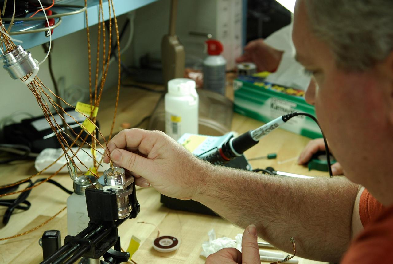 KENNEDY SPACE CENTER, FLA. -- At a lab at NASA's Kennedy Space Center, Bob Arp, an aerospace technician with the United Launch Alliance, inserts a wire from an electrical harness onto the pin of a replacement feed-through connector during preparations to solder the pins to the socket of the connector.  The connector will be installed in the external fuel tank for space shuttle Atlantis' STS-122 mission. The technician performed this exacting task on the Centaur upper stage for Atlas and Titan launches in 1994 and was specifically chosen for the task.   Soldering the connector pins and sockets together addresses the most likely cause of a problem in the engine cutoff sensor system, or ECO system.  Some of the tank's ECO sensors failed during propellant tanking for launch attempts on Dec. 6 and Dec. 9.  Results of a tanking test on Dec. 18 pointed to an open circuit in the feed-through connector wiring, which is located at the base of the tank. The feed-through connector passes the wires from the inside of the tank to the outside.  After the soldering is completed and the connector is reinstalled, shuttle program managers will decide on how to proceed.  The launch date for mission STS-122 is under review.  Photo credit: NASA/Kim Shiflett
