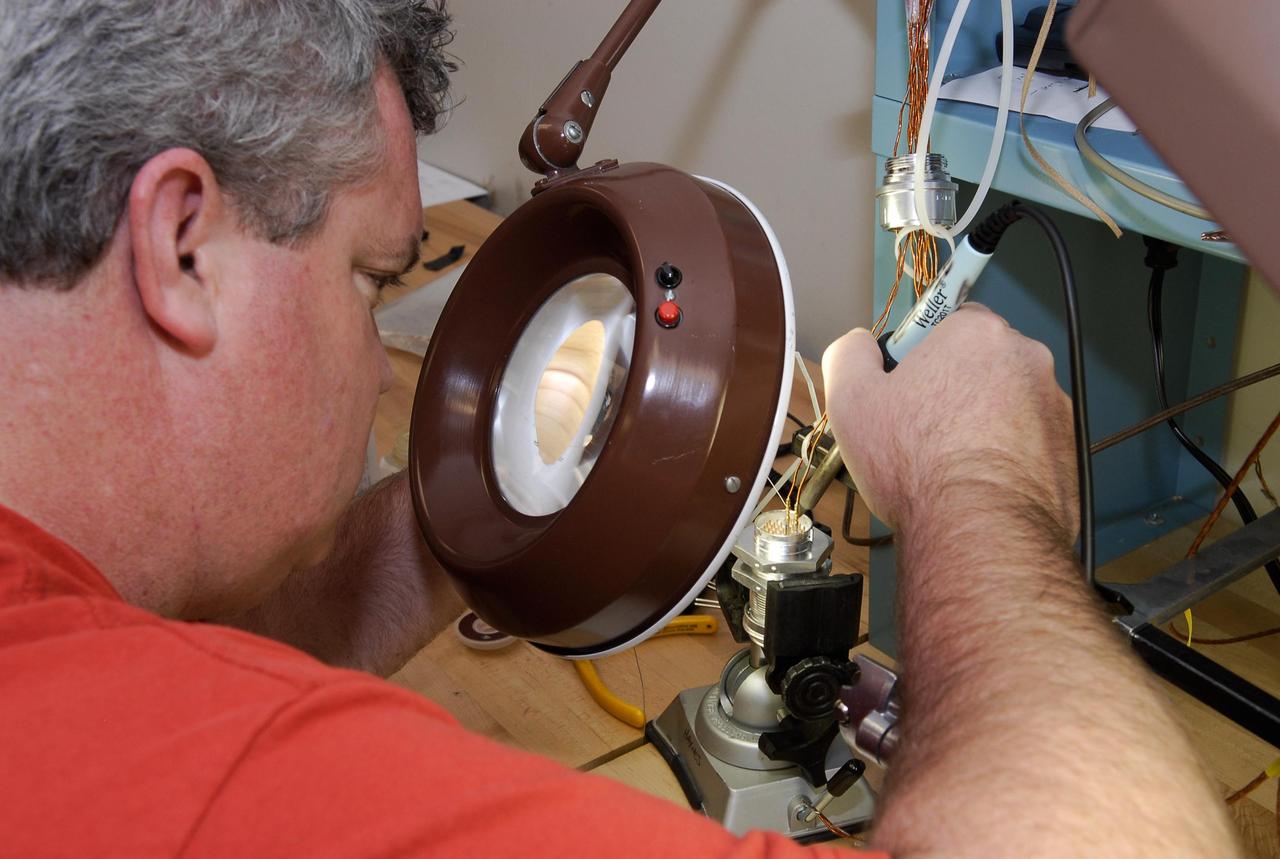 KENNEDY SPACE CENTER, FLA. -- At a lab at NASA's Kennedy Space Center, Bob Arp, an aerospace technician with the United Launch Alliance, solders a pin to the socket of the replacement feed-through connector that will be installed in the external fuel tank for space shuttle Atlantis' STS-122 mission. The technician performed this exacting task on the Centaur upper stage for Atlas and Titan launches in 1994 and was specifically chosen for the task. Soldering the connector pins and sockets together addresses the most likely cause of a problem in the engine cutoff sensor system, or ECO system. Some of the tank's ECO sensors failed during propellant tanking for launch attempts on Dec. 6 and Dec. 9. Results of a tanking test on Dec. 18 pointed to an open circuit in the feed-through connector wiring, which is located at the base of the tank. The feed-through connector passes the wires from the inside of the tank to the outside. After the soldering is completed and the connector is reinstalled, shuttle program managers will decide on how to proceed. The launch date for mission STS-122 is under review. Photo credit: NASA/Kim Shiflett