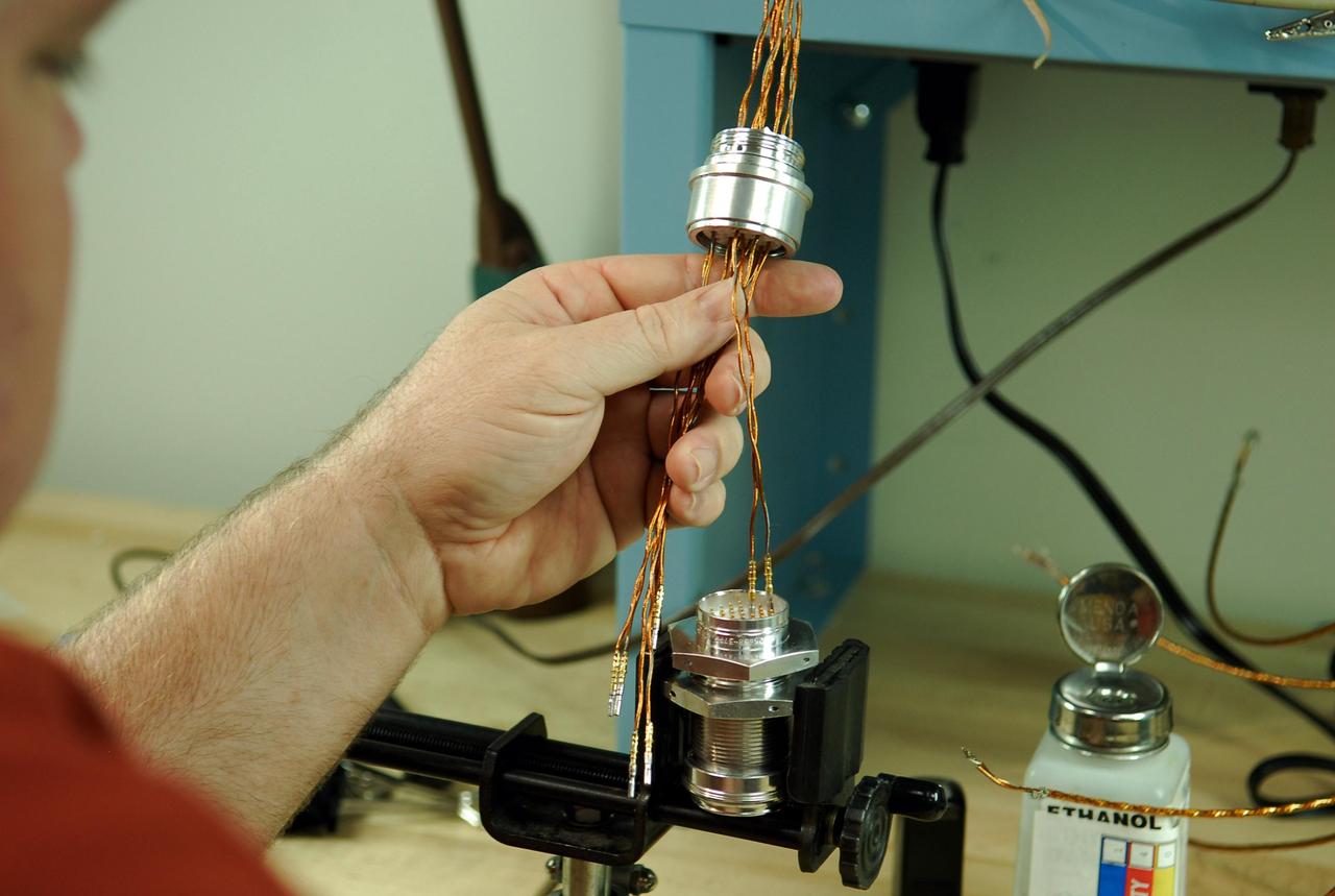 KENNEDY SPACE CENTER, FLA. -- At a lab at NASA's Kennedy Space Center, Bob Arp, an aerospace technician with the United Launch Alliance, examinies the pins remaining to be soldered to the socket of the replacement feed-through connector that will be installed in the external fuel tank for space shuttle Atlantis' STS-122 mission. The technician performed this exacting task on the Centaur upper stage for Atlas and Titan launches in 1994 and was specifically chosen for the task. Soldering the connector pins and sockets together addresses the most likely cause of a problem in the engine cutoff sensor system, or ECO system. Some of the tank's ECO sensors failed during propellant tanking for launch attempts on Dec. 6 and Dec. 9. Results of a tanking test on Dec. 18 pointed to an open circuit in the feed-through connector wiring, which is located at the base of the tank. The feed-through connector passes the wires from the inside of the tank to the outside. After the soldering is completed and the connector is reinstalled, shuttle program managers will decide on how to proceed. The launch date for mission STS-122 is under review. Photo credit: NASA/Kim Shiflett