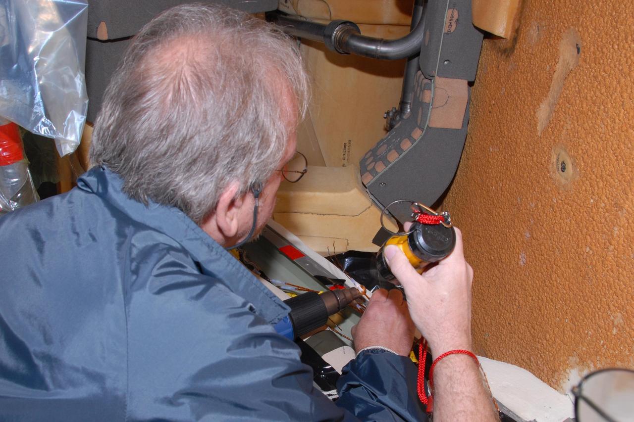 KENNEDY SPACE CENTER, FLA. -- On Launch Pad 39A, Lockheed Martin engineer Ray Clark splices wires between space shuttle Atlantis' external tank and the engine cutoff, or ECO, sensor system. The replacement feed-through connector in the ECO sensor system will be installed later. Some of the tank's ECO sensors gave failed readings during propellant tanking for Atlantis' STS-122 mission launch attempts on Dec. 6 and Dec. 9. Results of a tanking test on Dec. 18 pointed to an open circuit in the feed-through connector wiring, which is located at the base of the tank. The feed-through connector passes the wires from the inside of the tank to the outside. The pins in the replacement connector have been precisely soldered to create a connection that allows sensors inside the tank to send signals to the computers onboard Atlantis. No problems with the ECO sensors themselves have been found. NASA's Space Shuttle Program has proposed a target launch date of Feb. 7 for the STS-122 mission. That proposed launch date remains under evaluation pending coordination with all partners in the International Space Station Program. Photo credit: NASA/George Shelton