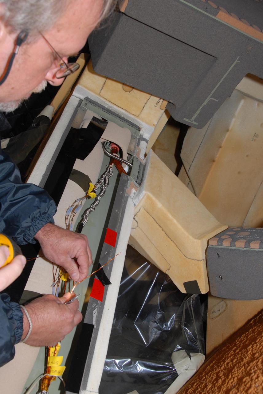 KENNEDY SPACE CENTER, FLA. -- On Launch Pad 39A, Lockheed Martin engineer Ray Clark splices wires between space shuttle Atlantis' external tank and the engine cutoff, or ECO, sensor system. The replacement feed-through connector in the ECO sensor system will be installed later. Some of the tank's ECO sensors gave failed readings during propellant tanking for Atlantis' STS-122 mission launch attempts on Dec. 6 and Dec. 9. Results of a tanking test on Dec. 18 pointed to an open circuit in the feed-through connector wiring, which is located at the base of the tank. The feed-through connector passes the wires from the inside of the tank to the outside. The pins in the replacement connector have been precisely soldered to create a connection that allows sensors inside the tank to send signals to the computers onboard Atlantis. No problems with the ECO sensors themselves have been found. NASA's Space Shuttle Program has proposed a target launch date of Feb. 7 for the STS-122 mission. That proposed launch date remains under evaluation pending coordination with all partners in the International Space Station Program. Photo credit: NASA/George Shelton