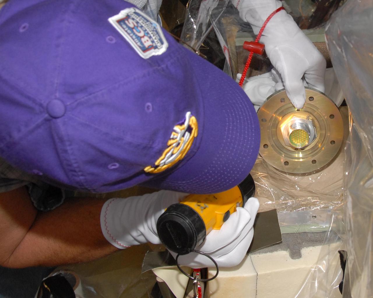 KENNEDY SPACE CENTER, FLA. --  Mike Berger, with Lockheed Martin, examines the replacement feed-through connector for the engine cutoff, or ECO, sensor system in space shuttle Atlantis' external tank.  The feed-through connector passes the wires from the inside of the tank to the outside.  Results of a tanking test on Dec. 18 pointed to an open circuit in the feed-through connector wiring, which is located at the base of the tank. The pins in the replacement connector have been precisely soldered to create a connection that allows sensors inside the tank to send signals to the computers onboard Atlantis. The work is being done on Launch Pad 39A.   Space shuttle Atlantis is now targeted for launch on Feb. 7.  Photo credit: NASA/George Shelton
