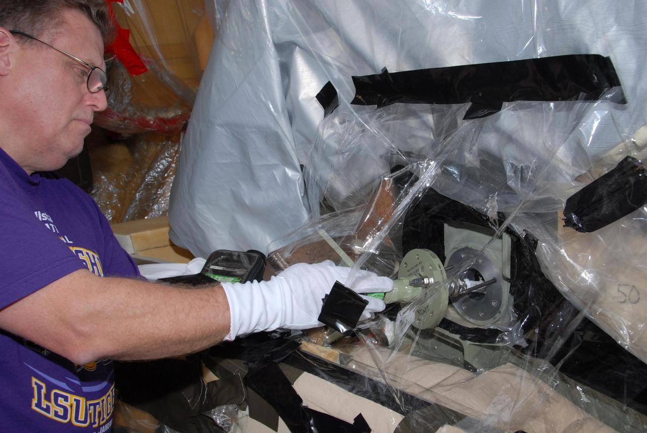 KENNEDY SPACE CENTER, FLA. --  Lloyd Johns, with Lockheed Martin, attaches the replacement feed-through connector in the engine cutoff, or ECO, sensor system to the internal connector on space shuttle Atlantis' external tank.  The feed-through connector passes the wires from the inside of the tank to the outside.  Results of a tanking test on Dec. 18 pointed to an open circuit in the feed-through connector wiring, which is located at the base of the tank. The pins in the replacement connector have been precisely soldered to create a connection that allows sensors inside the tank to send signals to the computers onboard Atlantis. The work is being done on Launch Pad 39A.   Space shuttle Atlantis is now targeted for launch on Feb. 7.  Photo credit: NASA/George Shelton