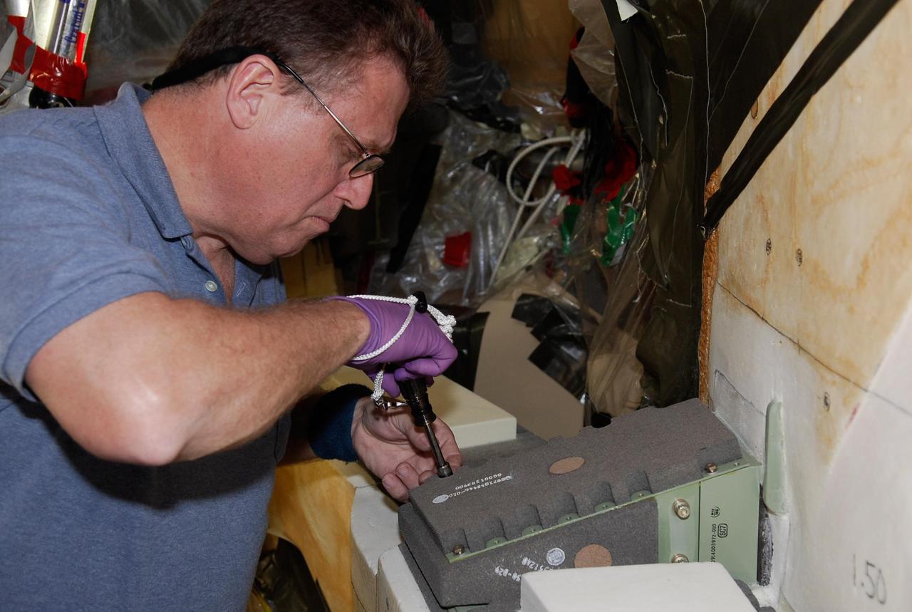 KENNEDY SPACE CENTER, FLA. --   On Launch Pad 39A at NASA's Kennedy Space Center, a technician attaches the cover over the engine cutoff, or ECO, sensor system connector and wiring on space shuttle Atlantis' external tank.  The feed-through connector passes the wires from the inside of the tank to the outside.  Results of a tanking test on Dec. 18 pointed to an open circuit in the feed-through connector wiring, which is located at the base of the tank. The pins in the replacement connector were precisely soldered to create a connection that allows sensors inside the tank to send signals to the computers onboard Atlantis.  The launch date for the shuttle's STS-122 mission has now been targeted for Feb. 7.   Photo credit: NASA/Kim Shiflett
