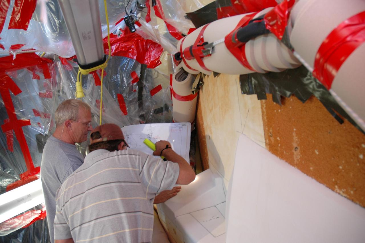 KENNEDY SPACE CENTER, FLA. --  Quality inspectors with NASA and Lockheed Martin examine a red-line drawing of foam placement on space shuttle Atlantis's external tank (in front of them) to verify the foam insulation that was reapplied.  The foam covers the feed-through engine cut-off, or ECO, sensor connector.  The foam was removed to enable engineers to remove and replace the ECO sensor connector on the tank.  The feed-through connector passes the wires from the inside of the tank to the outside.  Results of a tanking test on Dec. 18 pointed to an open circuit in the feed-through connector wiring, which is located at the base of the tank. The pins in the replacement connector were precisely soldered to create a connection that allows sensors inside the tank to send signals to the computers onboard Atlantis.  The repair work was done on Atlantis while the shuttle has been on Launch Pad 39A at NASA's Kennedy Space Center.  The launch date for the shuttle's STS-122 mission has now been targeted for Feb. 7.   Photo credit: NASA/Cory Husten
