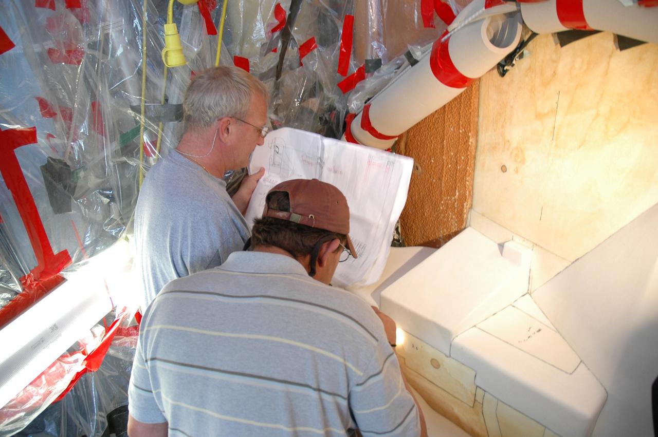 KENNEDY SPACE CENTER, FLA. --  Quality inspectors with NASA and Lockheed Martin examine a red-line drawing of foam placement on space shuttle Atlantis's external tank (in front of them) to verify the foam insulation that was reapplied.  The foam covers the feed-through engine cut-off, or ECO, sensor connector.  The foam was removed to enable engineers to remove and replace the ECO sensor connector on the tank.  The feed-through connector passes the wires from the inside of the tank to the outside.  Results of a tanking test on Dec. 18 pointed to an open circuit in the feed-through connector wiring, which is located at the base of the tank. The pins in the replacement connector were precisely soldered to create a connection that allows sensors inside the tank to send signals to the computers onboard Atlantis.  The repair work was done on Atlantis while the shuttle has been on Launch Pad 39A at NASA's Kennedy Space Center.  The launch date for the shuttle's STS-122 mission has now been targeted for Feb. 7.   Photo credit: NASA/Cory Husten
