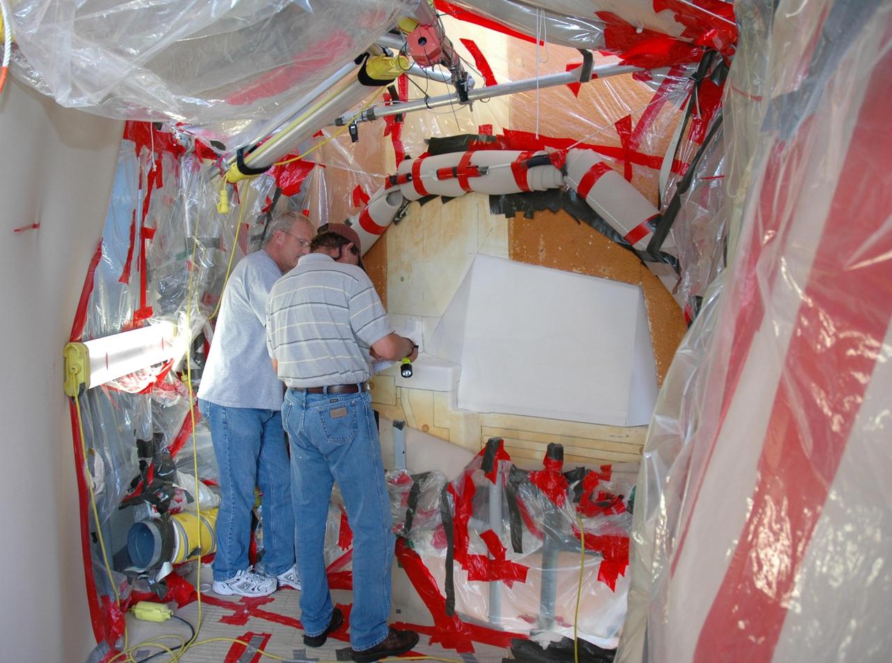 KENNEDY SPACE CENTER, FLA. --  Quality inspectors with NASA and Lockheed Martin examine a red-line drawing of foam placement on space shuttle Atlantis's external tank (in front of them) to verify the foam insulation that was reapplied.  The foam covers the feed-through engine cut-off, or ECO, sensor connector.  The foam was removed to enable engineers to remove and replace the ECO sensor connector on the tank.  The feed-through connector passes the wires from the inside of the tank to the outside.  Results of a tanking test on Dec. 18 pointed to an open circuit in the feed-through connector wiring, which is located at the base of the tank. The pins in the replacement connector were precisely soldered to create a connection that allows sensors inside the tank to send signals to the computers onboard Atlantis.  The repair work was done on Atlantis while the shuttle has been on Launch Pad 39A at NASA's Kennedy Space Center.  The launch date for the shuttle's STS-122 mission has now been targeted for Feb. 7.   Photo credit: NASA/Cory Husten