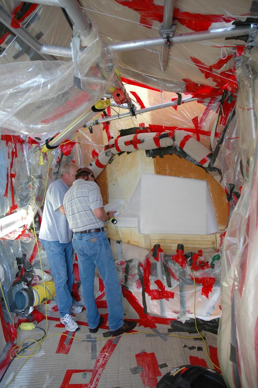 KENNEDY SPACE CENTER, FLA. --  Quality inspectors with NASA and Lockheed Martin examine a red-line drawing of foam placement on space shuttle Atlantis's external tank (in front of them) to verify the foam insulation that was reapplied.  The foam covers the feed-through engine cut-off, or ECO, sensor connector.  The foam was removed to enable engineers to remove and replace the ECO sensor connector on the tank.  The feed-through connector passes the wires from the inside of the tank to the outside.  Results of a tanking test on Dec. 18 pointed to an open circuit in the feed-through connector wiring, which is located at the base of the tank. The pins in the replacement connector were precisely soldered to create a connection that allows sensors inside the tank to send signals to the computers onboard Atlantis.  The repair work was done on Atlantis while the shuttle has been on Launch Pad 39A at NASA's Kennedy Space Center.  The launch date for the shuttle's STS-122 mission has now been targeted for Feb. 7.   Photo credit: NASA/Cory Husten