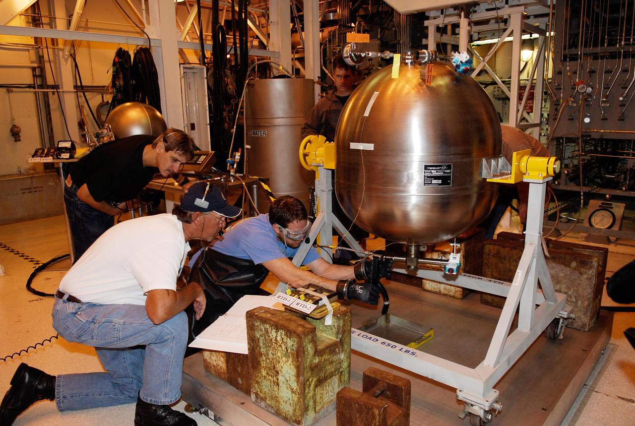 KENNEDY SPACE CENTER, FLA. -- In the hypergolic maintenance facility at NASA's Kennedy Space Center, a technician (right) adjusts equipment during testing of the Ares I-X Roll Control System, or RoCS. The RoCS Servicing Simulation Test is to gather data that will be used to help certify the ground support equipment design and validate the servicing requirements and processes. The RoCS is part of the Interstage structure, the lowest axial segment of the Upper Stage Simulator. In an effort to reduce costs and meet the schedule, most of the ground support equipment that will be used for the RoCS servicing is of space shuttle heritage. This high-fidelity servicing simulation will provide confidence that servicing requirements can be met with the heritage system. At the same time, the test will gather process data that will be used to modify or refine the equipment and processes to be used for the actual flight element. Photo credit: NASA/Kim Shiflett