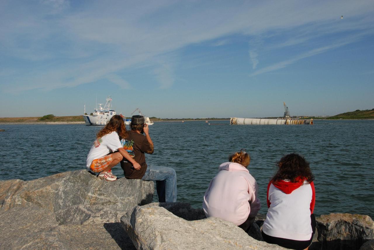 KENNEDY SPACE CENTER, FLA. -- Spectators watch as the solid rocket booster retrieval ship Freedom Star tows one of the boosters, retrieved after the launch of space shuttle Atlantis' STS-122 mission, toward Port Canaveral.  The space shuttle's solid rocket booster casings and associated flight hardware are recovered at sea. The boosters impact the Atlantic Ocean approximately seven minutes after liftoff. The splashdown area is a square of about 6 by 9 nautical miles located about 140 nautical miles downrange from the launch pad. The retrieval ships are stationed approximately 8 to 10 nautical miles from the impact area at the time of splashdown. As soon as the boosters enter the water, the ships accelerate to a speed of 15 knots and quickly close on the boosters. The pilot chutes and main parachutes are the first items to be brought on board. With the chutes and frustum recovered, attention turns to the boosters. The ship's tow line is connected and the booster is returned to the Port and, after transfer to a position alongside the ship, to Hangar AF at Cape Canaveral Air Force Station. There, the expended boosters are disassembled, refurbished and reloaded with solid propellant for reuse.  Photo credit: NASA/Jack Pfaller
