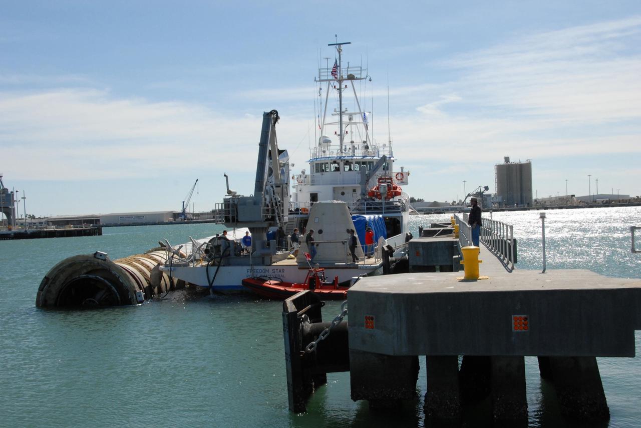 KENNEDY SPACE CENTER, FLA. -- The solid rocket booster retrieval ship Freedom Star is temporarily docked at Port Canaveral while the booster it was towing is moved alongside for the remainder of the trip upriver to Cape Canaveral Air Force Station.  Freedom Star retrieved the booster after the launch of space shuttle Atlantis' STS-122 mission. The space shuttle's solid rocket booster casings and associated flight hardware are recovered at sea. The boosters impact the Atlantic Ocean approximately seven minutes after liftoff. The splashdown area is a square of about 6 by 9 nautical miles located about 140 nautical miles downrange from the launch pad. The retrieval ships are stationed approximately 8 to 10 nautical miles from the impact area at the time of splashdown. As soon as the boosters enter the water, the ships accelerate to a speed of 15 knots and quickly close on the boosters. The pilot chutes and main parachutes are the first items to be brought on board. With the chutes and frustum recovered, attention turns to the boosters. The ship's tow line is connected and the booster is returned to the Port and, after transfer to a position alongside the ship, to Hangar AF at Cape Canaveral Air Force Station. There, the expended boosters are disassembled, refurbished and reloaded with solid propellant for reuse.  Photo credit: NASA/Jack Pfaller