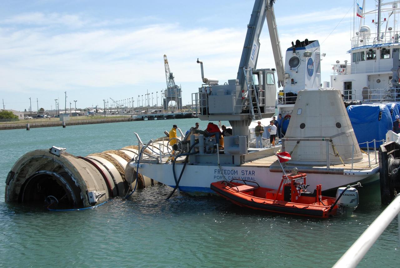 KENNEDY SPACE CENTER, FLA. -- The solid rocket booster retrieval ship Freedom Star is temporarily docked at Port Canaveral while the booster it was towing is moved alongside for the remainder of the trip upriver to Cape Canaveral Air Force Station.  Freedom Star retrieved the booster after the launch of space shuttle Atlantis' STS-122 mission.  The space shuttle's solid rocket booster casings and associated flight hardware are recovered at sea. The boosters impact the Atlantic Ocean approximately seven minutes after liftoff. The splashdown area is a square of about 6 by 9 nautical miles located about 140 nautical miles downrange from the launch pad. The retrieval ships are stationed approximately 8 to 10 nautical miles from the impact area at the time of splashdown. As soon as the boosters enter the water, the ships accelerate to a speed of 15 knots and quickly close on the boosters. The pilot chutes and main parachutes are the first items to be brought on board. With the chutes and frustum recovered, attention turns to the boosters. The ship's tow line is connected and the booster is returned to the Port and, after transfer to a position alongside the ship, to Hangar AF at Cape Canaveral Air Force Station. There, the expended boosters are disassembled, refurbished and reloaded with solid propellant for reuse.  Photo credit: NASA/Jack Pfaller