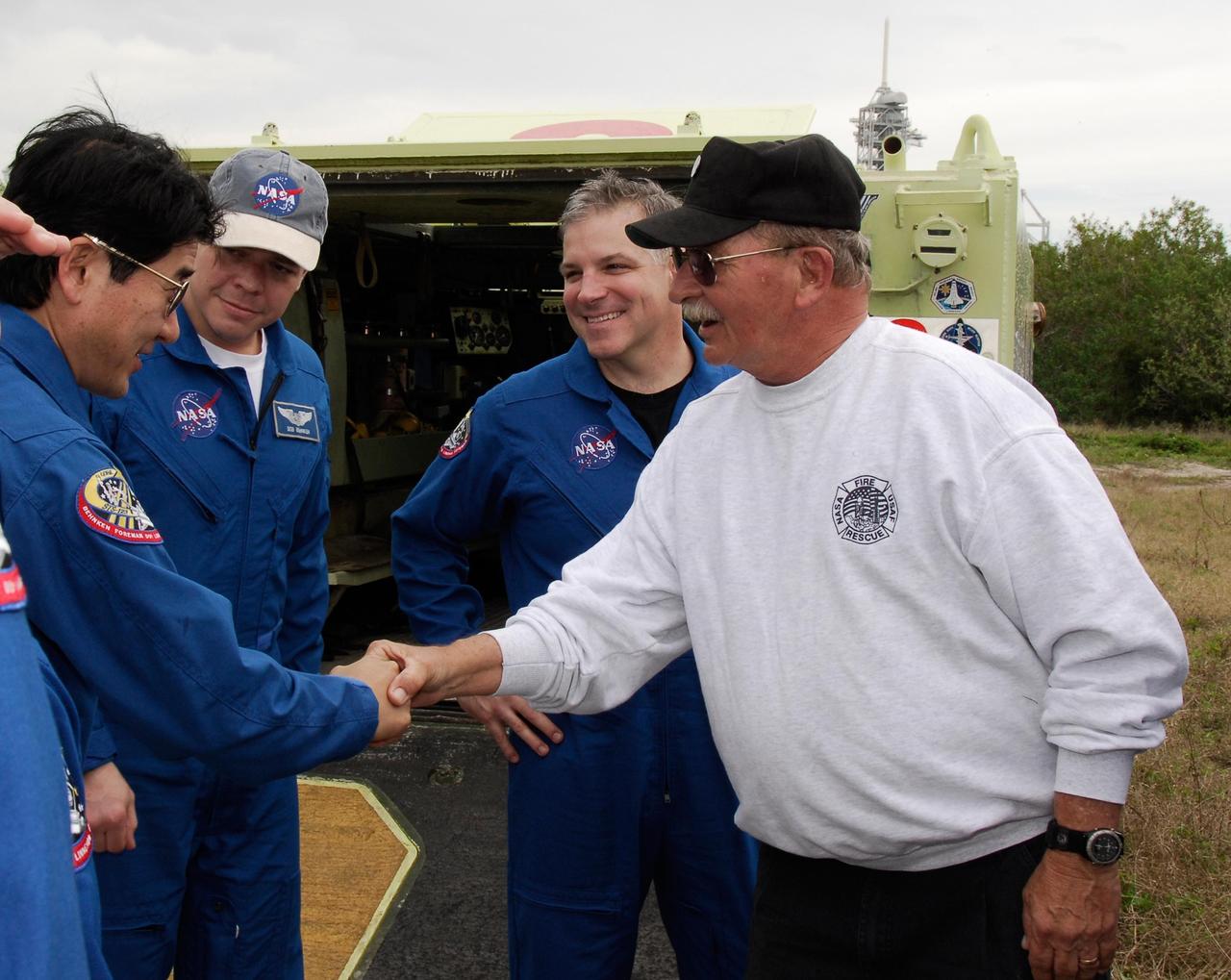 KENNEDY SPACE CENTER, FLA. -- At NASA Kennedy Space Center's Launch Complex 39, astronaut rescue team leader Capt. George Hoggard, at right, greets STS-123 Mission Specialist Takao Doi of the Japan Aerospace Exploration Agency as fellow crew members, from left, Mission Specialist Robert L. Behnken and Pilot Gregory H. Johnson look on.  The crew for space shuttle Endeavour's STS-123 mission will practice driving the M-113 armored personnel carrier, in the background, part of their training on emergency egress procedures.  An M-113 will be available to transport the crew to safety in the event of a contingency on the pad before their launch.  The STS-123 crew is at Kennedy for a full launch dress rehearsal, known as the terminal countdown demonstration test or TCDT.  Endeavour's seven astronauts arrived at Kennedy's Shuttle Landing Facility in their T-38 training aircraft between 10:45 and 10:58 a.m. EST. The terminal countdown demonstration test provides astronauts and ground crews with an opportunity to participate in various simulated countdown activities, including equipment familiarization and emergency training. Endeavour is targeted to launch March 11 at 2:28 a.m. EDT on a 16-day mission to the International Space Station. On the mission, Endeavour and its crew will deliver the first section of the Japan Aerospace Exploration Agency's Kibo laboratory and the Canadian Space Agency's two-armed robotic system, Dextre. Photo credit: NASA/Kim Shiflett