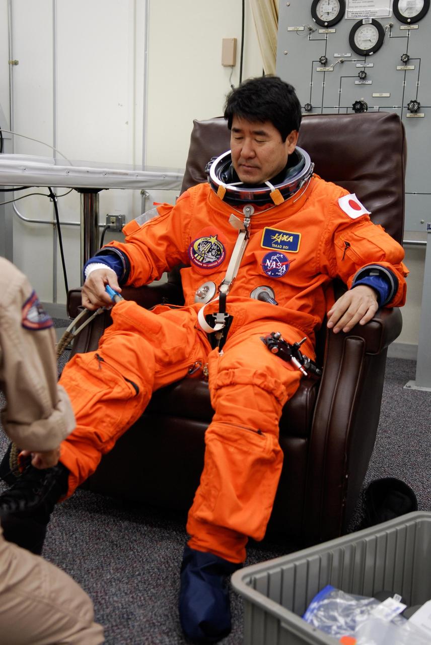 KENNEDY SPACE CENTER, FLA. --  STS-123 Mission Specialist Takao Doi is helped with his boots during suitup for the launch dress rehearsal, culmination of the terminal countdown demonstration test, or TCDT. Doi represents the Japan Aerospace and Exploration Agency, or JAXA. The TCDT provides astronauts and ground crews with an opportunity to participate in various simulated countdown activities, including equipment familiarization and emergency training. Space shuttle Endeavour is targeted to launch March 11 at 2:28 a.m. EDT on the 16-day STS-123 mission to the International Space Station.  Endeavour and its crew will deliver the first section of the Japan Aerospace Exploration Agency's Kibo laboratory and the Canadian Space Agency's two-armed robotic system, Dextre.   Photo credit: NASA/Kim Shiflett