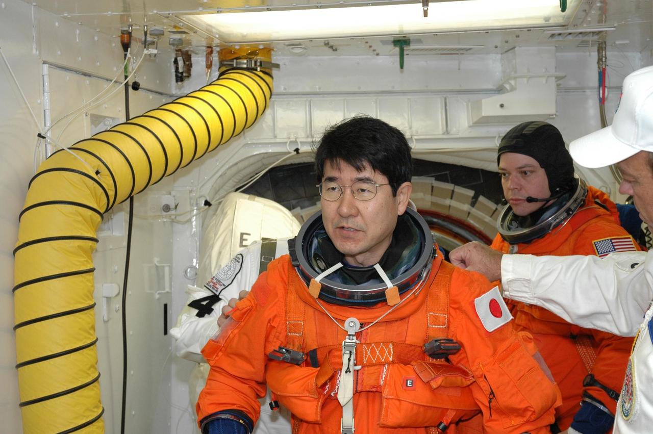 KENNEDY SPACE CENTER, FLA. -- In the White Room on NASA Kennedy Space Center's Launch Pad 39A, STS-123 Mission Specialist Takao Doi, who represents the Japan Aerospace Exploration Agency, gets help with his launch and entry suit before entering space shuttle Endeavour. Behind him is Mission Specialist Robert L. Behnken. Both are getting ready for the simulated launch countdown, which is the culmination of the terminal countdown demonstration test, or TCDT. The TCDT provides astronauts and ground crews with an opportunity to participate in various countdown activities, including equipment familiarization and emergency egress training. Endeavour is targeted to launch at 2:28 a.m. EDT March 11 on the 16-day STS-123 mission to the International Space Station. Endeavour and its crew will deliver the first section of the Japan Aerospace Exploration Agency's Kibo laboratory and the Canadian Space Agency's two-armed robotic system, Dextre. Photo credit: NASA/Jim Grossmann