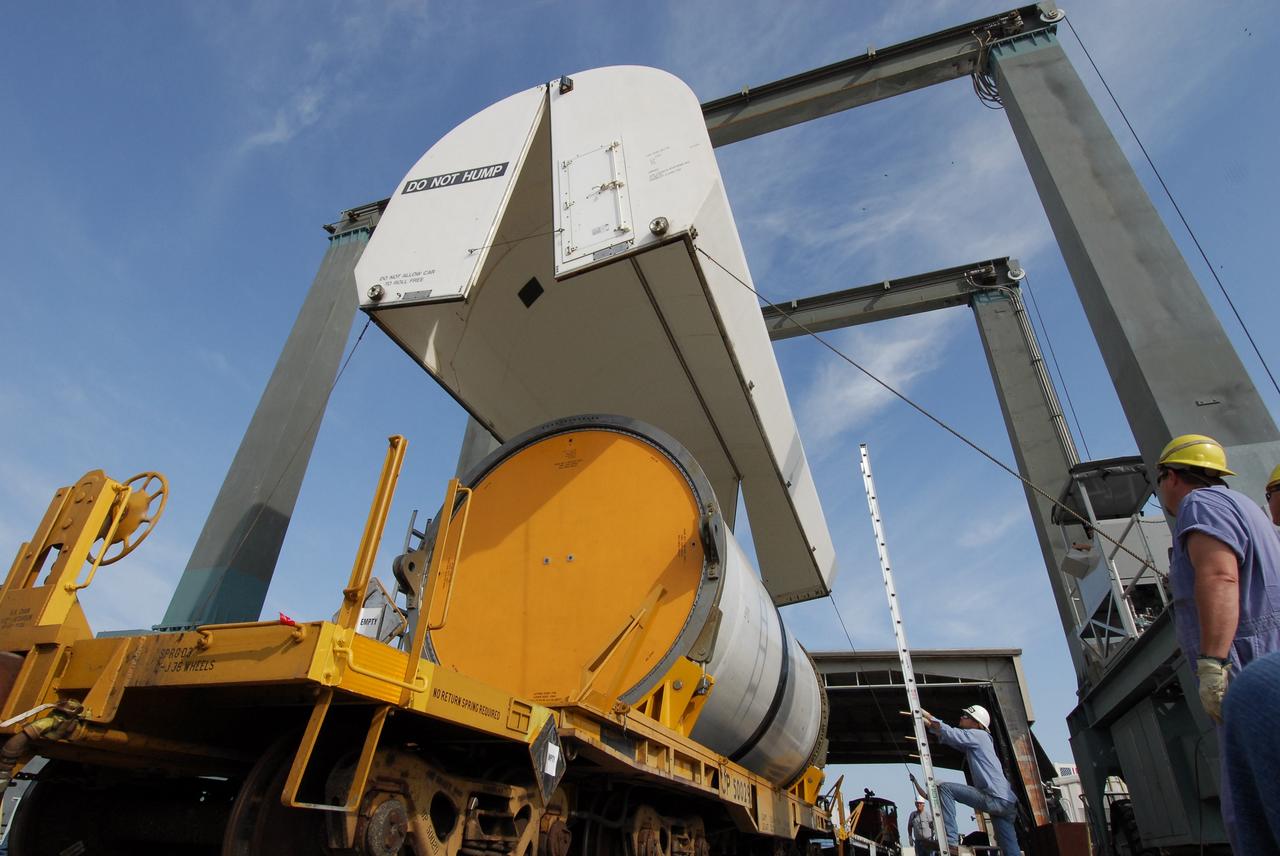 KENNEDY SPACE CENTER, FLA. --  At the NASA Railroad yard at NASA's Kennedy Space Center, workers lower a transportation cover over another solid rocket booster segment from the STS-122 mission.  Loaded on the railroad cars, the segments will be transported to Utah. After a mission, the spent boosters are recovered, cleaned, disassembled, refurbished and reused after each launch. After hydrolasing the interior of each segment, they are placed on flatbed trucks. The individual booster segments are transferred to a railhead located at the railroad yard.  The covered segments will be moved to Titusville for interchange with Florida East Coast Railway to begin the trip back to the Thiokol plant in Wa¬satch, Utah.   Photo credit: NASA/Jack Pfaller