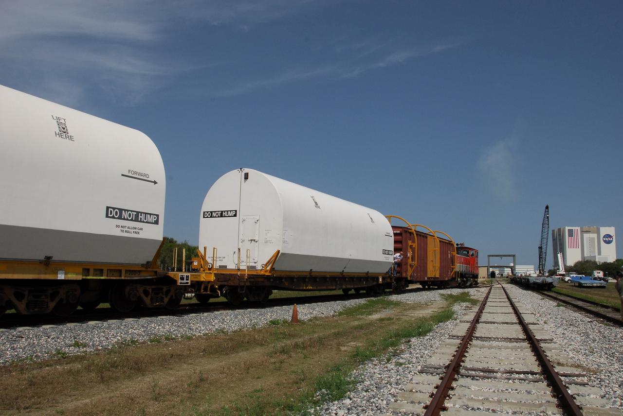 KENNEDY SPACE CENTER, FLA. --  The NASA Railroad train moves along the track through NASA's Kennedy Space Center.  In the distance, at right, is the Vehicle Assembly Building. The train is hauling the solid rocket booster segments from the STS-122 mission.  After a mission, the spent boosters are recovered, cleaned, disassembled, refurbished and reused after each launch. After hydrolasing the interior of each segment, they are placed on flatbed trucks. The individual booster segments are transferred to a railhead located at the railroad yard.  The covered segments will be moved to Titusville for interchange with Florida East Coast Railway to begin the trip back to the Thiokol plant in Wa¬satch, Utah.   Photo credit: NASA/Jack Pfaller