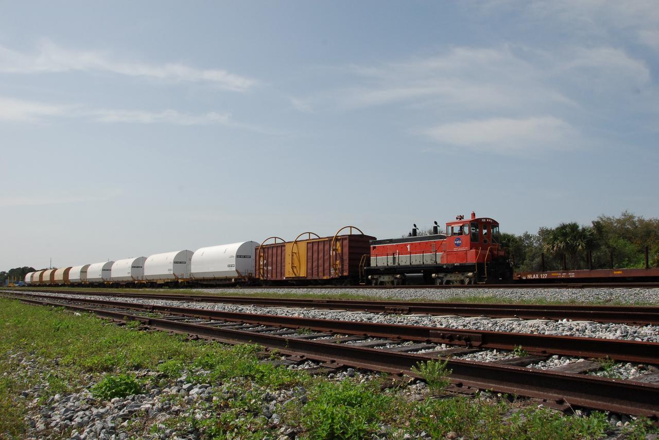 KENNEDY SPACE CENTER, FLA. --  The NASA Railroad train moves along the track through NASA's Kennedy Space Center.  The train is hauling the solid rocket booster segments from the STS-122 mission.  After a mission, the spent boosters are recovered, cleaned, disassembled, refurbished and reused after each launch. After hydrolasing the interior of each segment, they are placed on flatbed trucks. The individual booster segments are transferred to a railhead located at the railroad yard.  The covered segments will be moved to Titusville for interchange with Florida East Coast Railway to begin the trip back to the Thiokol plant in Wa¬satch, Utah.   Photo credit: NASA/Jack Pfaller