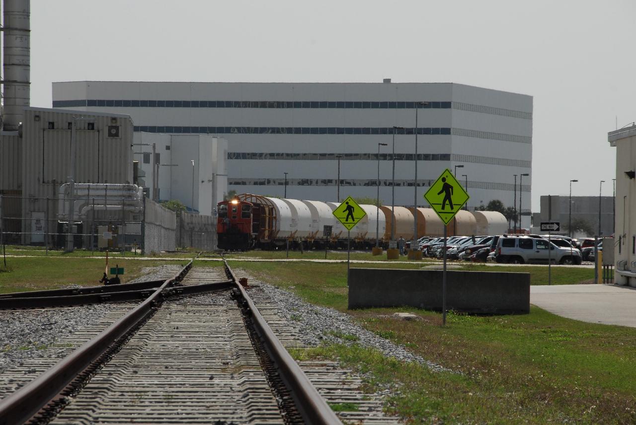 KENNEDY SPACE CENTER, FLA. --  The NASA Railroad train moves along the track through NASA's Kennedy Space Center.  Behind it is the Operations and Support Building I in the Launch Complex 39 Area.  The train is hauling the solid rocket booster segments from the STS-122 mission. After a mission, the spent boosters are recovered, cleaned, disassembled, refurbished and reused after each launch. After hydrolasing the interior of each segment, they are placed on flatbed trucks. The individual booster segments are transferred to a railhead located at the railroad yard.  The covered segments will be moved to Titusville for interchange with Florida East Coast Railway to begin the trip back to the Thiokol plant in Wa¬satch, Utah.   Photo credit: NASA/Jack Pfaller