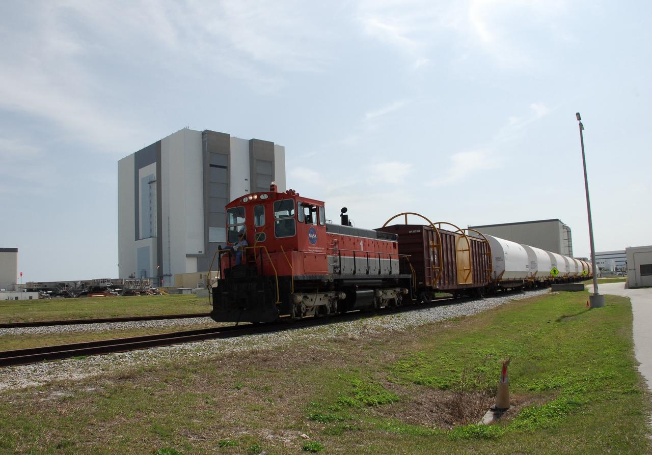 KENNEDY SPACE CENTER, FLA. --   The NASA Railroad train moves along the track through NASA Kennedy Space Center's Launch Complex 39 Area.  Behind the locomotive car is the Vehicle Assembly Building. The train is hauling the solid rocket booster segments from the STS-122 mission.  After a mission, the spent boosters are recovered, cleaned, disassembled, refurbished and reused after each launch. After hydrolasing the interior of each segment, they are placed on flatbed trucks. The individual booster segments are transferred to a railhead located at the railroad yard.  The covered segments will be moved to Titusville for interchange with Florida East Coast Railway to begin the trip back to the Thiokol plant in Wa¬satch, Utah.   Photo credit: NASA/Jack Pfaller