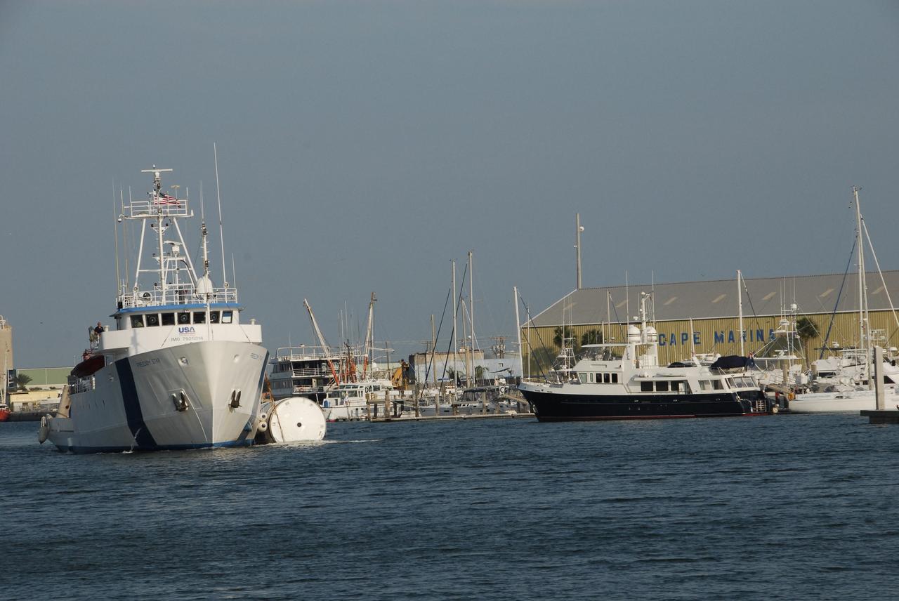 KENNEDY SPACE CENTER, FLA. --  The Freedom Star, one of NASA's solid rocket booster retrieval ships, motors through Port Canaveral with a solid rocket booster alongside. The booster is from space shuttle Endeavour, which launched the STS-123 mission on March 11. The space shuttle’s solid rocket booster casings and associated flight hardware are recovered at sea. The boosters impact the Atlantic Ocean approximately seven minutes after liftoff. The splashdown area is a square of about 6 by 9 nautical miles located about 140 nautical miles downrange from the launch pad. The retrieval ships are stationed approximately 8 to 10 nautical miles from the impact area at the time of splashdown. As soon as the boosters enter the water, the ships accelerate to a speed of 15 knots and quickly close on the boosters, which they tow back to port.  After transfer to a position alongside the ship, the booster will be towed  to Hangar AF at Cape Canaveral Air Force Station. There, the expended boosters are disassembled, refurbished and reloaded with solid propellant for reuse.   Photo credit: NASA/Jack Pfaller
